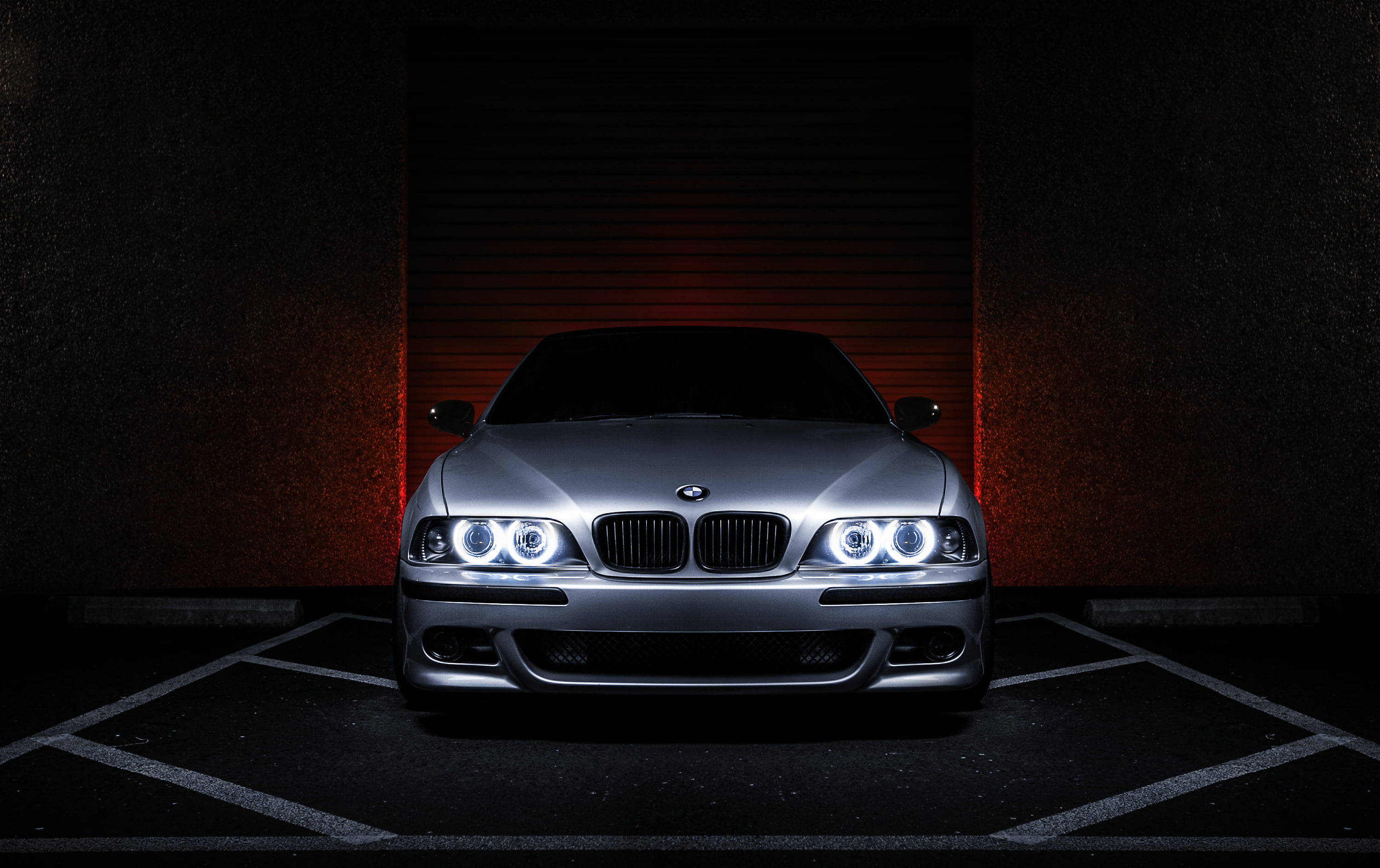 銀色 5 系列 BMW 電腦壁紙 壁紙 — 一輛銀色寶馬跑車，車頭燈閃爍，停放在昏暗的車庫中，帶有紅色背光。