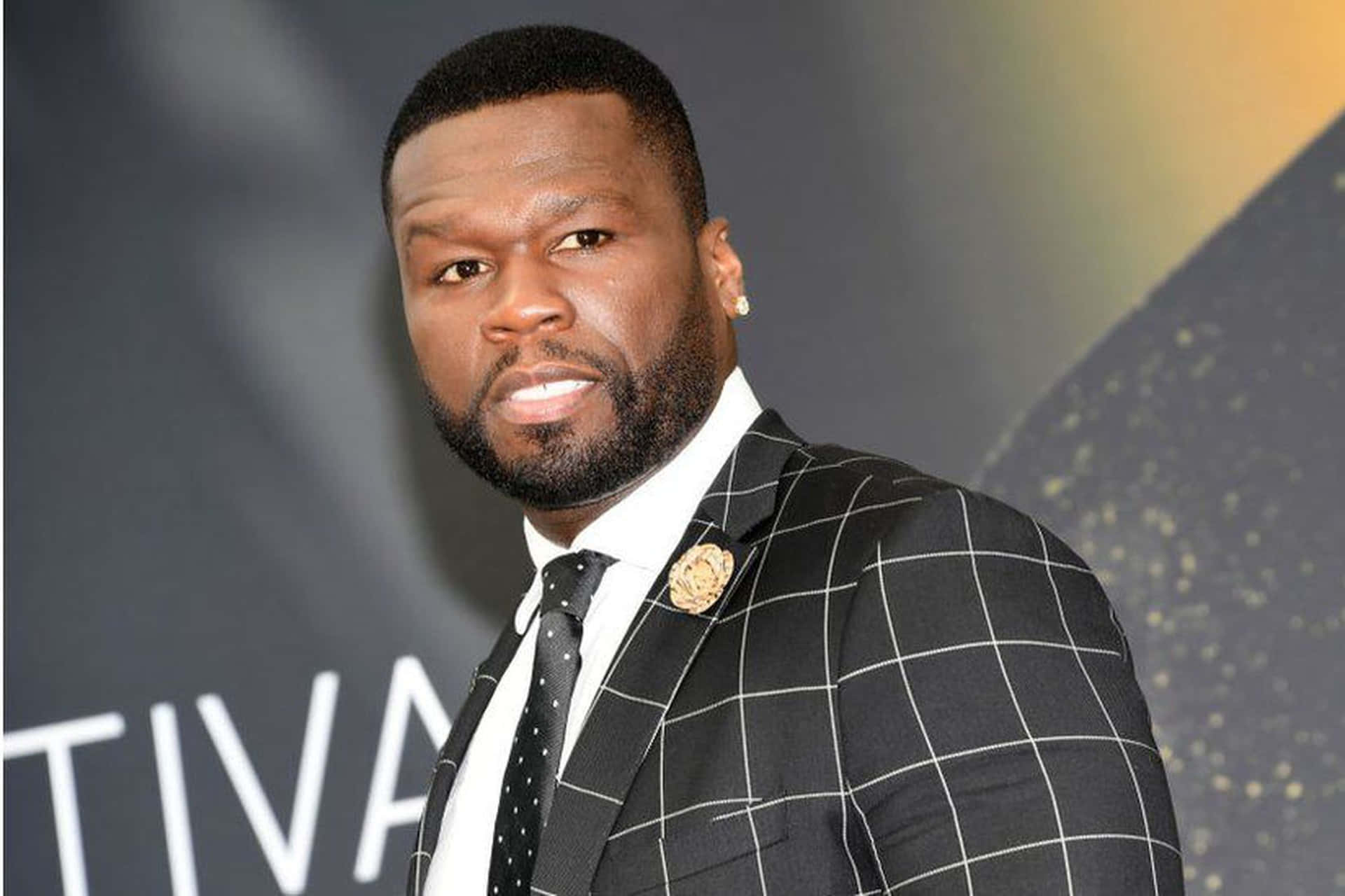 50 Cent 在活動中身穿黑色格紋西裝，佩戴金色領針。