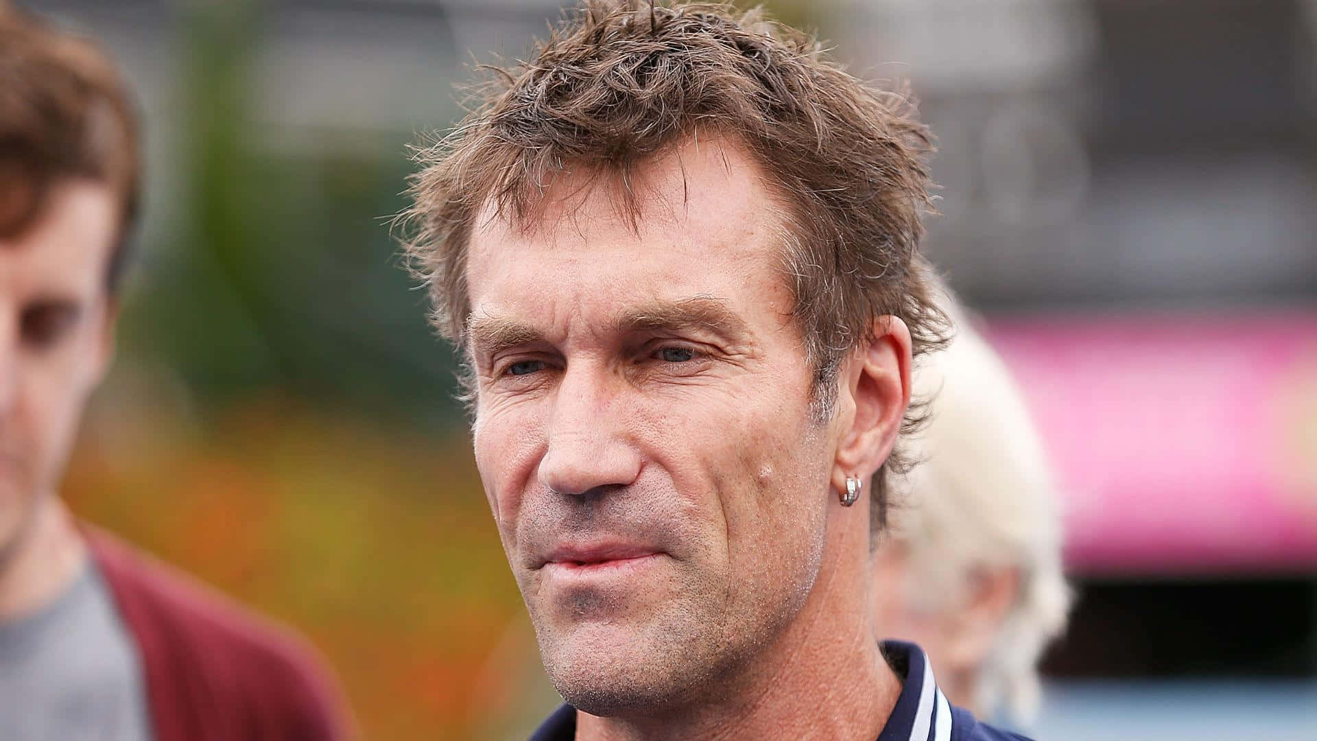 58 歲溫布頓冠軍 Pat Cash 壁紙 — 一名棕色亂髮、帶著微妙微笑、視線稍微偏離鏡頭的男士特寫肖像。