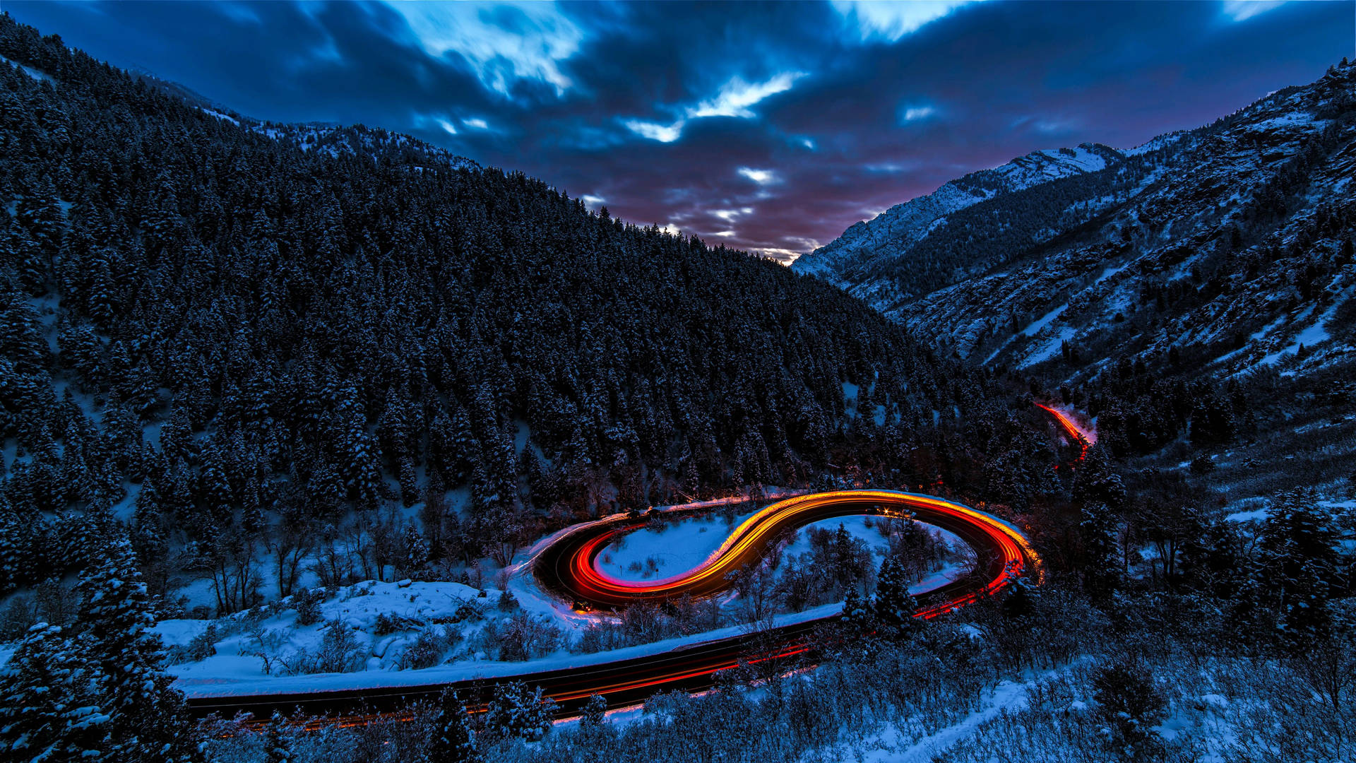 黃昏時分蜿蜒的山路，汽車光跡穿過雪林閃閃發光。