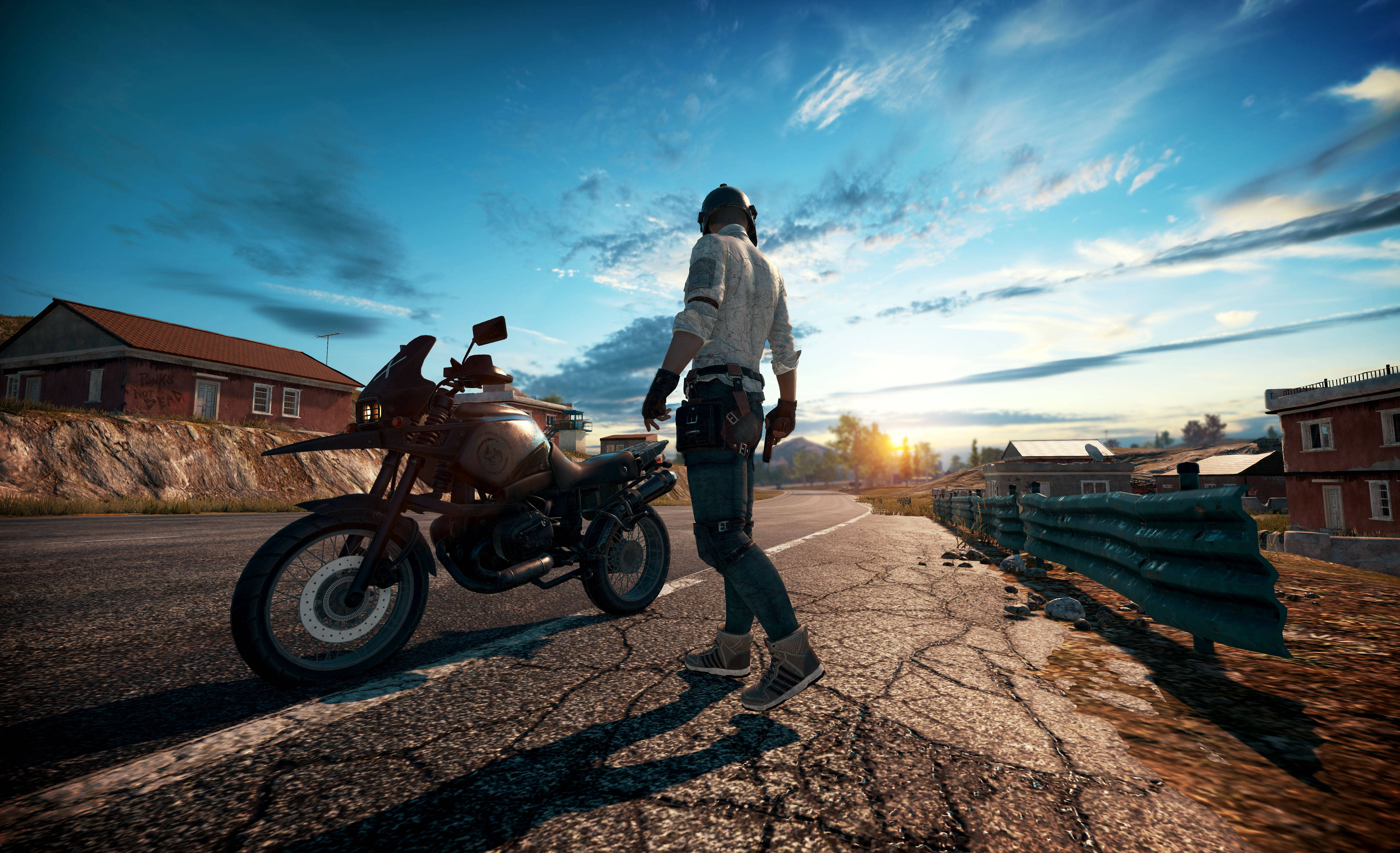 5K高清PUBG摩托車 壁紙 — 一位戴頭盔穿牛仔褲的孤獨騎士，在金色日落時分，沿著一條裂縫的道路，走在一輛堅固的電單車旁邊。