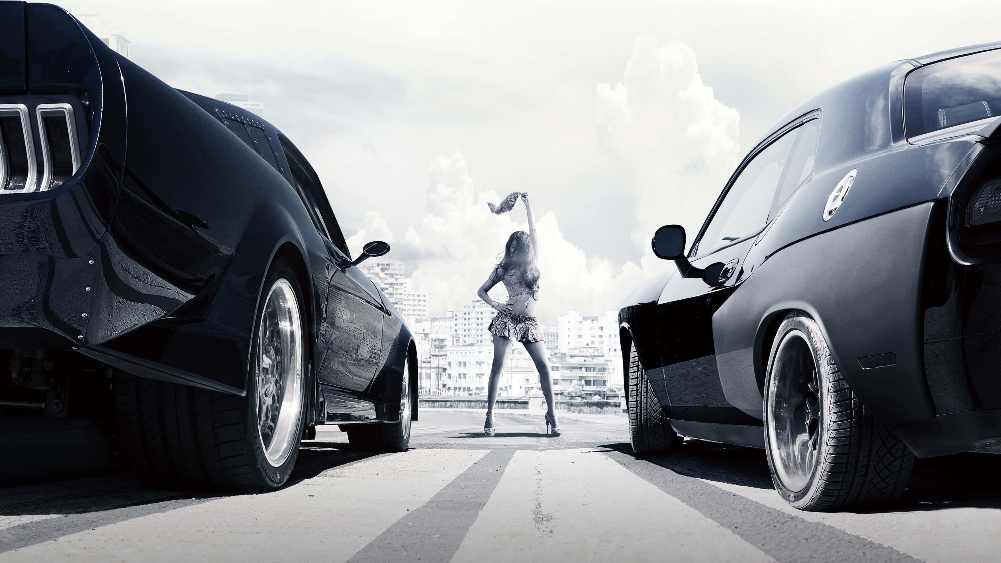 《速度與激情6》經典賽車場景：福特野馬與道奇挑戰者 壁紙 — 一位穿著短裙的女性自信地站在兩輛黑色肌肉車之間，背景是鋪砌的停車場和多雲的天空。