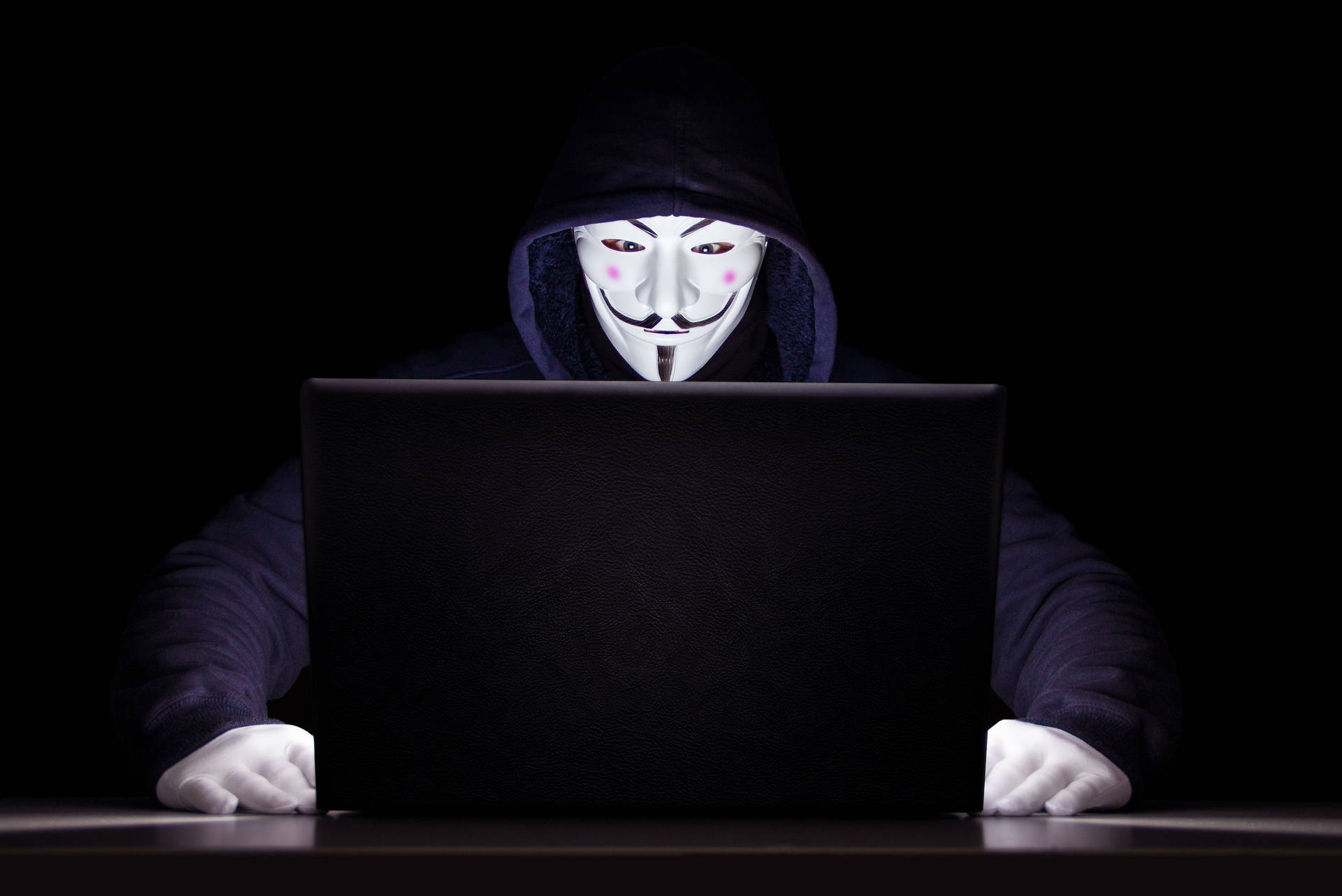 戴著蓋伊·福克斯面具的匿名人士在黑暗房間中使用筆記本電腦。