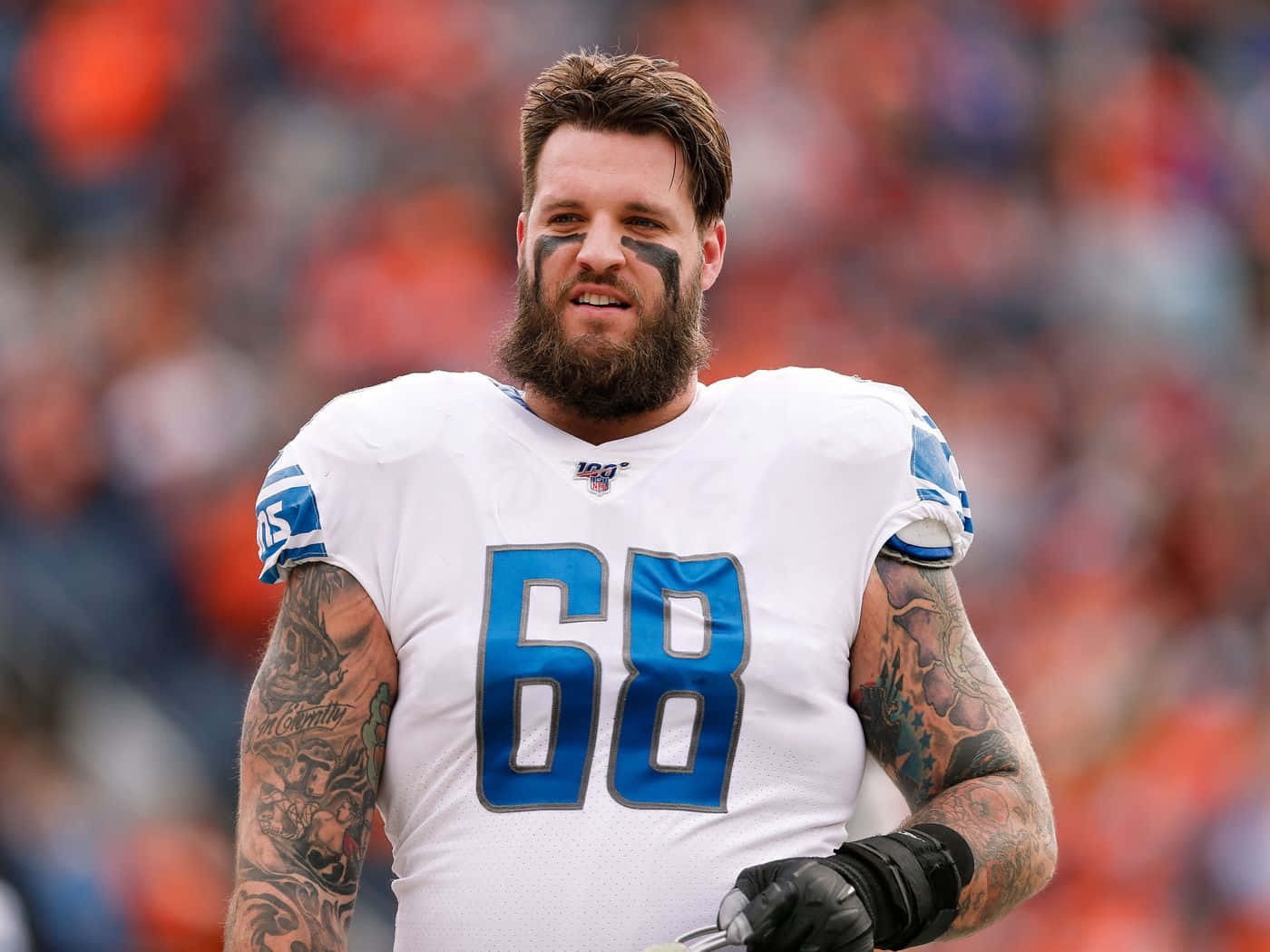 68號足球攻防鋒線泰勒·德克爾 壁紙 — 一位留鬍子的NFL進攻截鋒，身穿白色球衣，藍色68號碼，站在球場上，手臂上的紋身清晰可見。