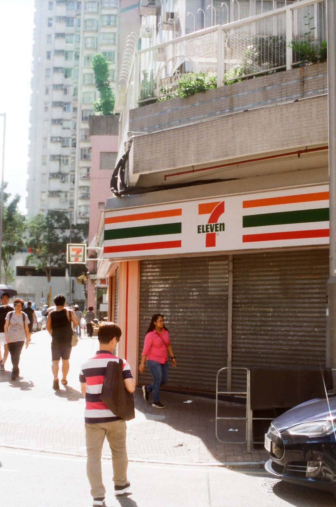 行人在陽光明媚的城市街道上經過一間關閉的7-Eleven商店。