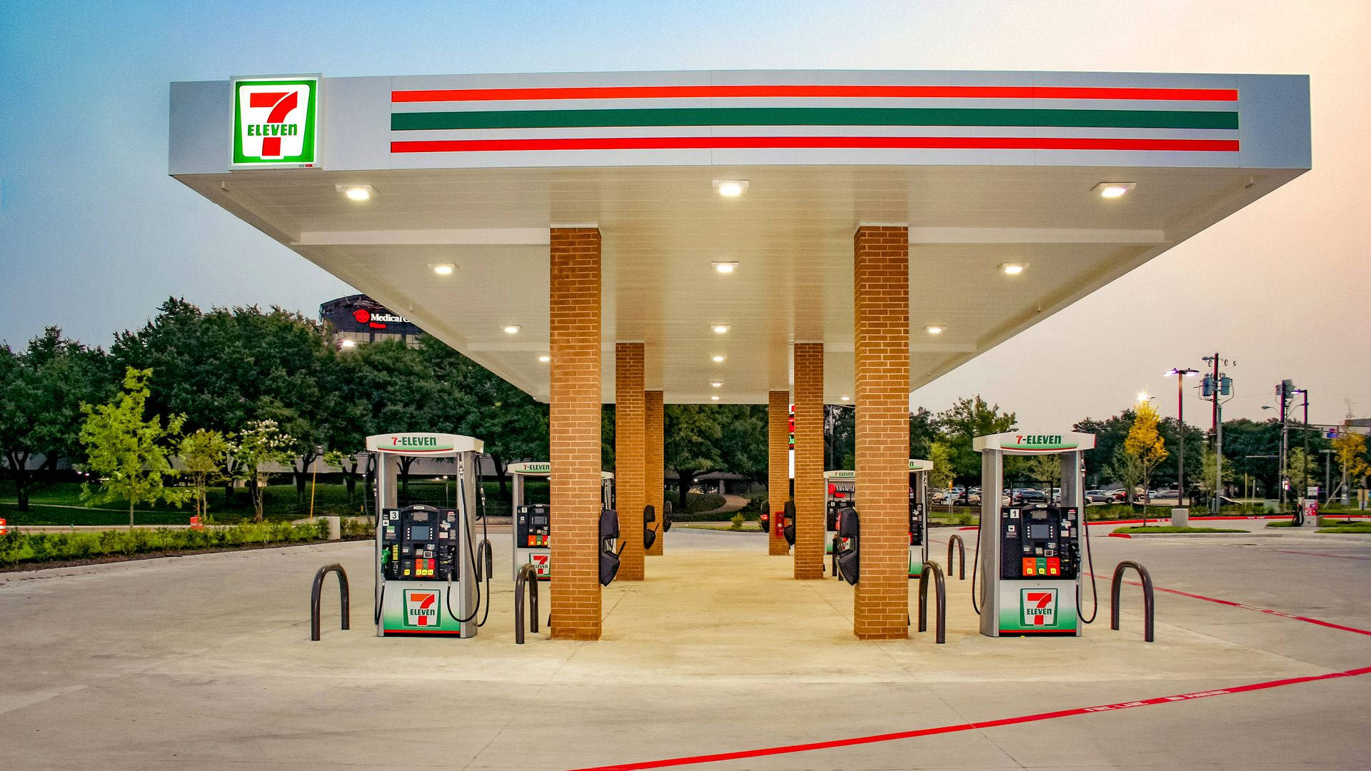 7-Eleven加油站 壁紙 — 一間7 eleven加油站，採用紅、綠、白品牌色調，背景是暮色天空和樹木。