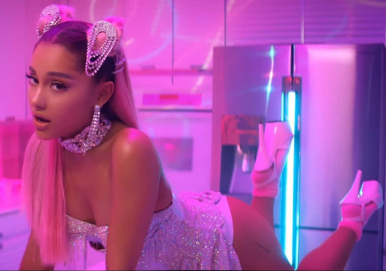 愛莉安娜·格蘭德在《7 Rings》音樂錄影帶中展現強勢風采 壁紙 — Ariana Grande 身穿閃亮粉紅服裝，戴著鑽石貓耳，靠著未來廚房中的霓虹燈冰箱。