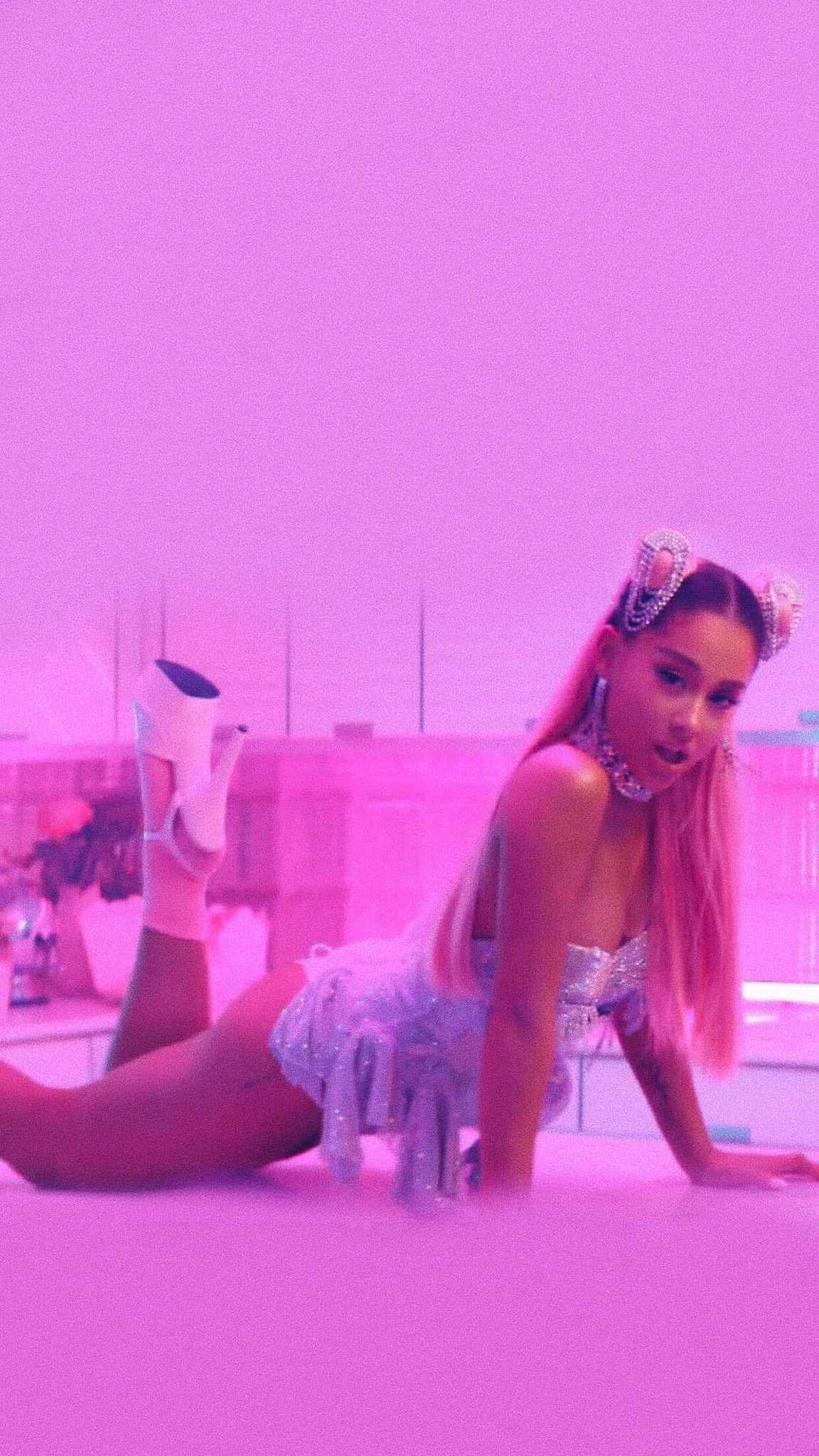 愛莉安娜·格蘭德展示熱門單曲《7 Rings》 壁紙 — 一位粉紅色頭髮、穿著閃亮服裝的女性在粉紅色屋頂上，在霓虹粉紅燈光下擺姿勢。