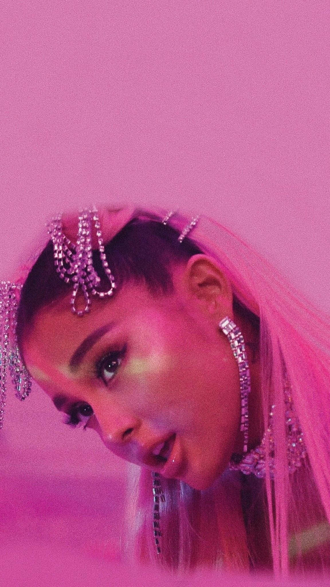 愛莉安娜·格蘭德展示《7 Rings》七枚戒指 壁紙 — 亞莉安娜·格蘭德（Ariana Grande）在單色粉紅背景下，佩戴閃爍的鑽石头飾和粉紅面紗，凝視著鏡頭。