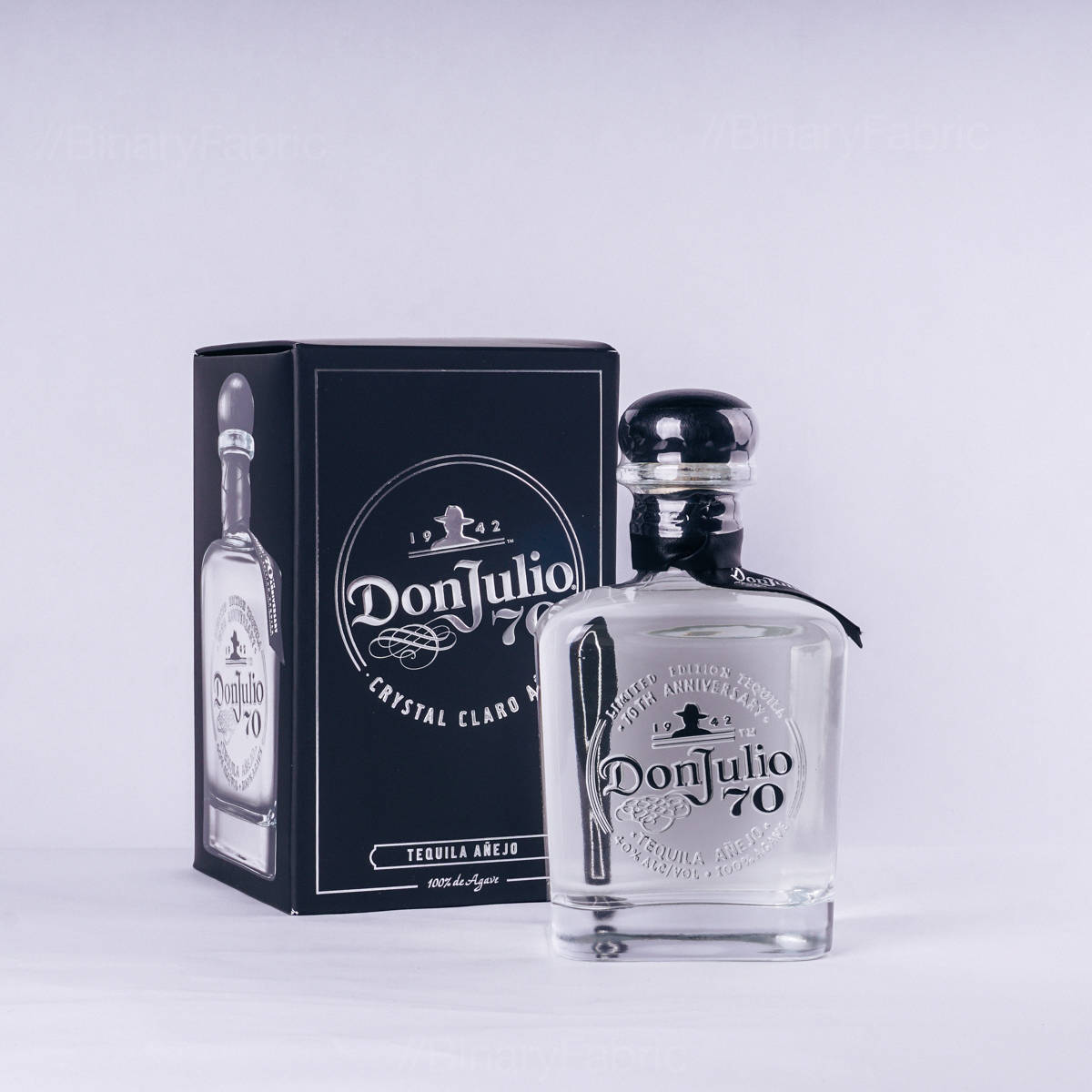 唐·胡里奧70號龍舌蘭酒 壁紙 — 一個透明玻璃瓶的Don Julio 70龍舌蘭酒放在其黑色盒子旁邊，背景為純白色。
