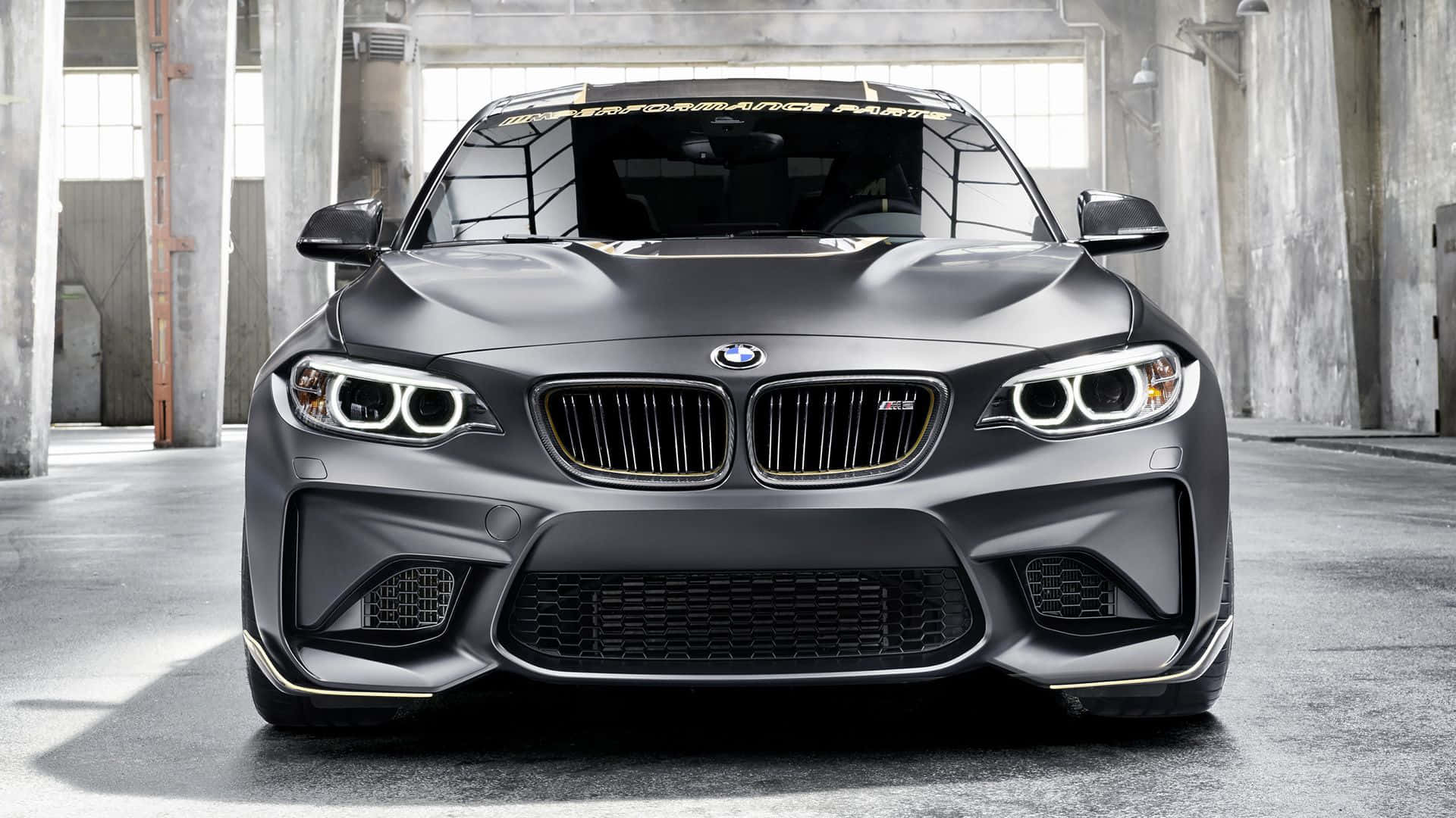 混凝土倉庫內帶金色飾邊的啞光灰色BMW M2跑車。