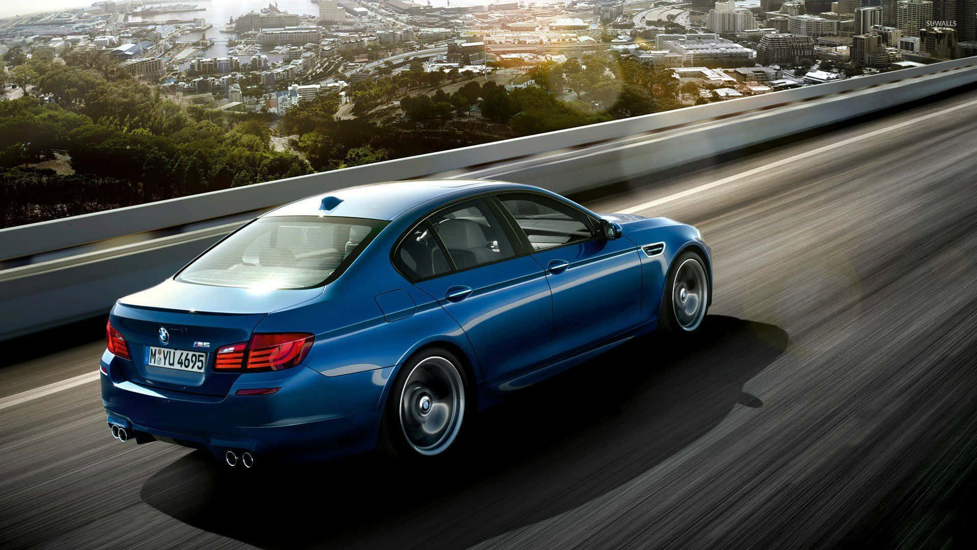 日落時分，藍色BMW M5在高速公路上行駛，背景有城市和樹木。