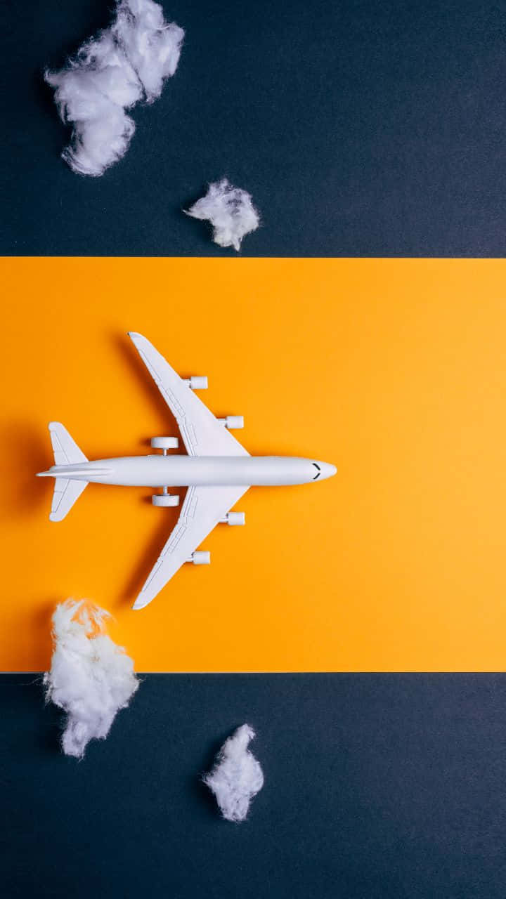 720p 旅行背景：飛機模型 壁紙 — 一架白色玩具飛機放在一條大膽的橙色條紋上，兩側是深藍色，周圍散落著蓬鬆的棉花雲。