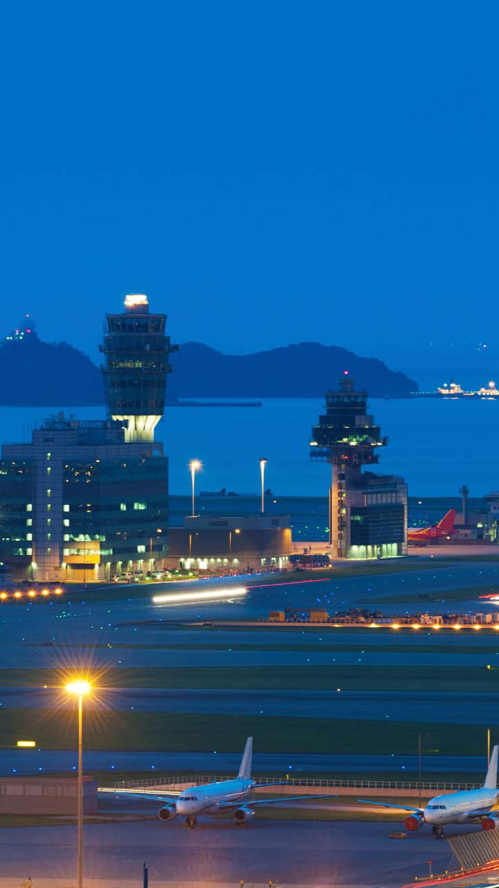 720p旅行背景 - 香港國際機場夜景 壁紙 — 深藍色天空下，暮色中機場的鳥瞰圖，發光的控制塔和停機坪上的飛機。