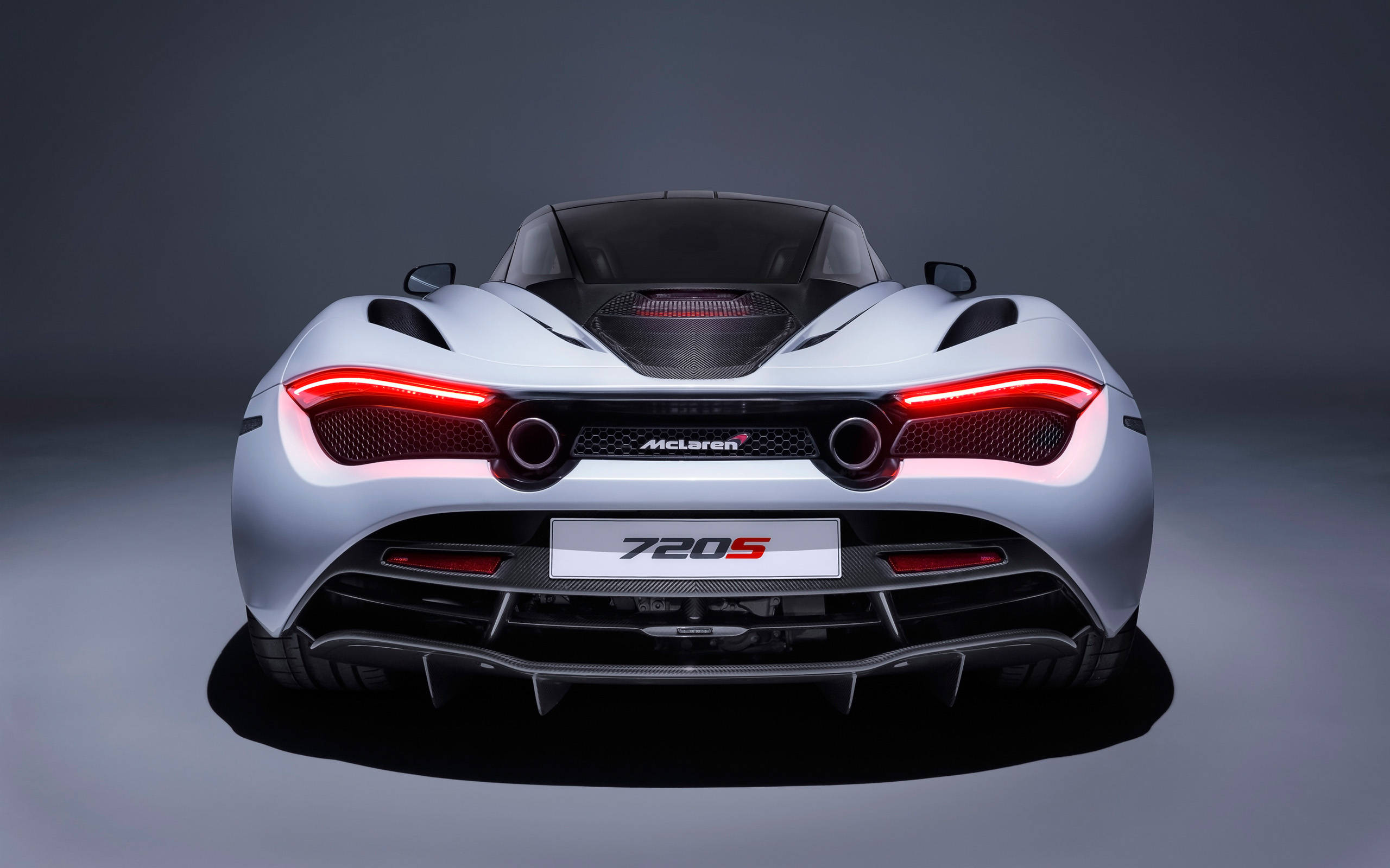 銀色超跑麥拉倫720s 4K 壁紙 — 一輛時尚的銀色McLaren 720S跑車，從後方觀看，帶有發光的紅色尾燈，背景為深色工作室。