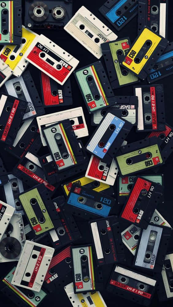 80年代彩色錄音帶 iPhone 壁紙 — 一張充滿活力的俯拍照片，展示散落的復古錄音帶，色彩鮮明，背景深色。