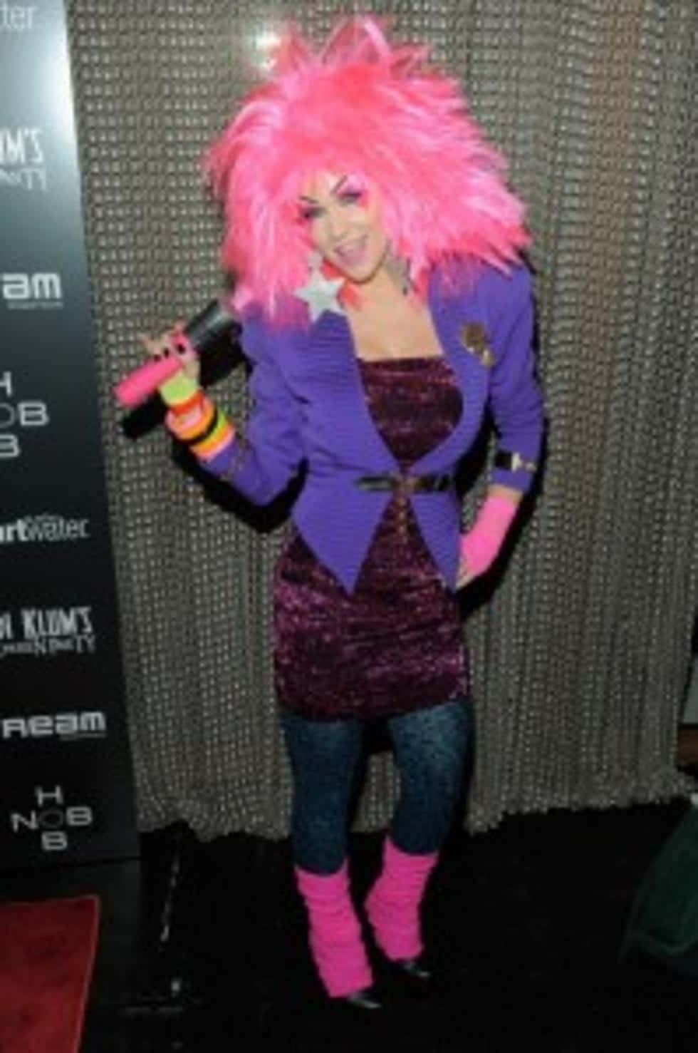 戴粉色假髮穿紫色服裝的人在活動中拿著麥克風。