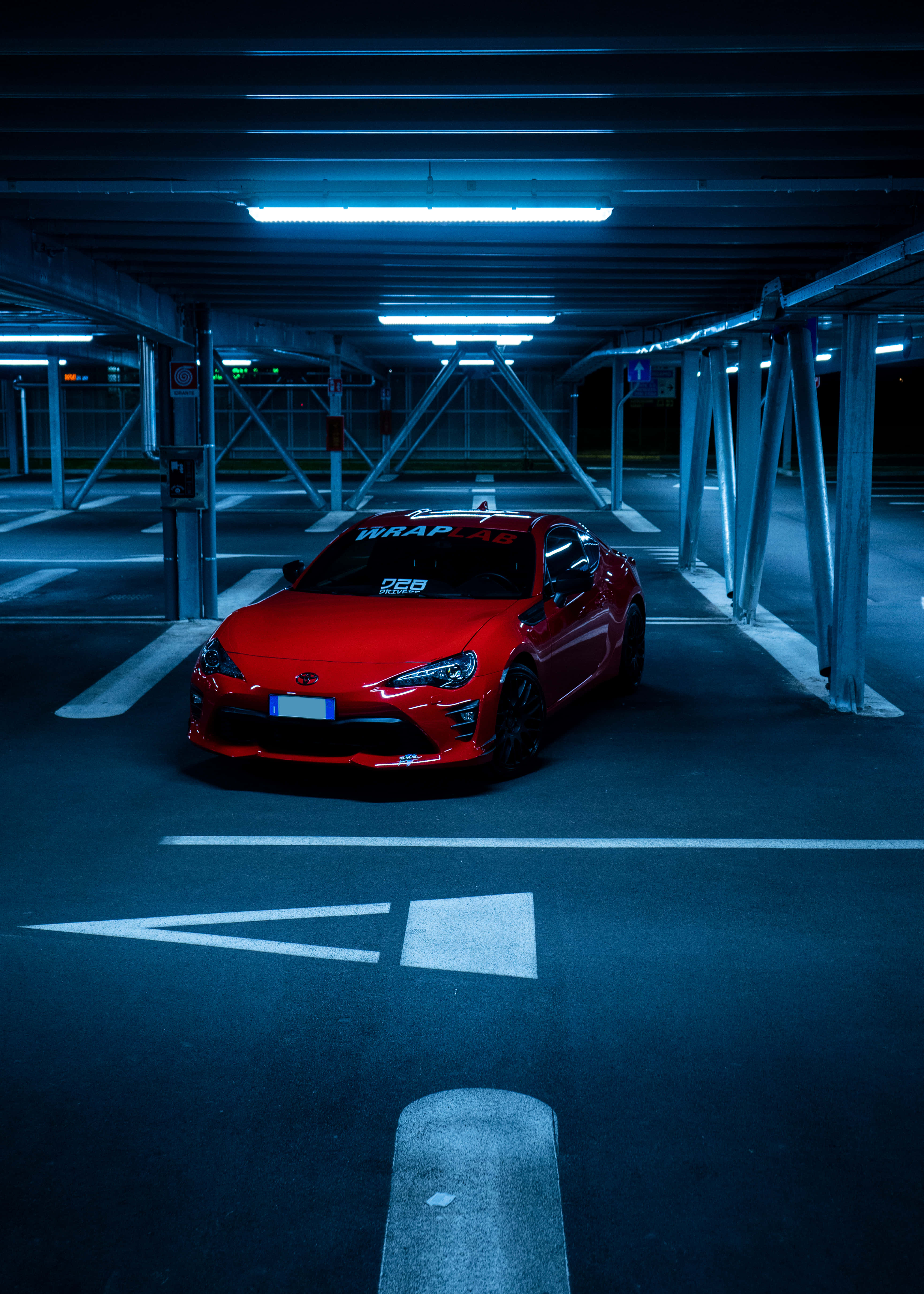 感受豐田86的動力與速度 壁紙 — 一輛鮮紅色跑車在夜晚空無一人的地下停車場中，在清涼的藍色螢光燈下閃閃發光。