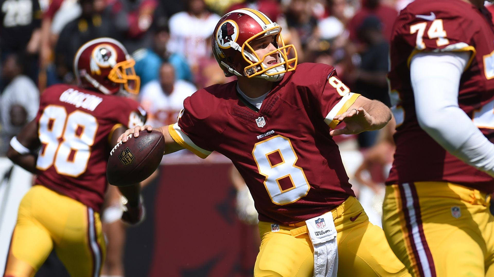 8號球員 Kirk Cousins 壁紙 — 華盛頓美式足球隊的四分衛身穿棗紅色和金色球衣，在陽光明媚的日間比賽中與隊友一起擲出美式足球。