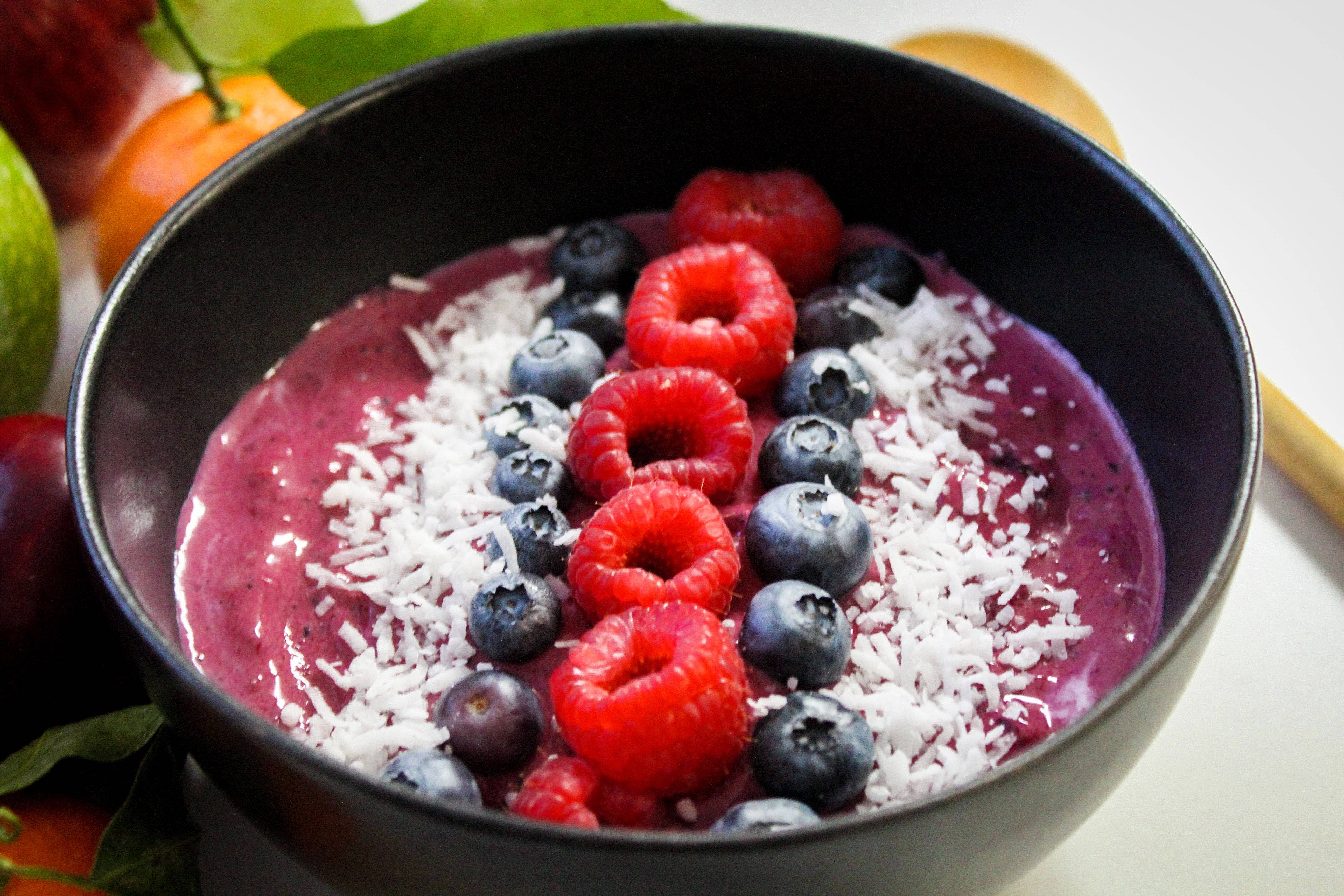 açai 藍莓果實碗特寫 壁紙 — 一個充滿活力的紫色冰沙碗，上面放有覆盆子、藍莓和椰絲，盛載於黑色碗中。