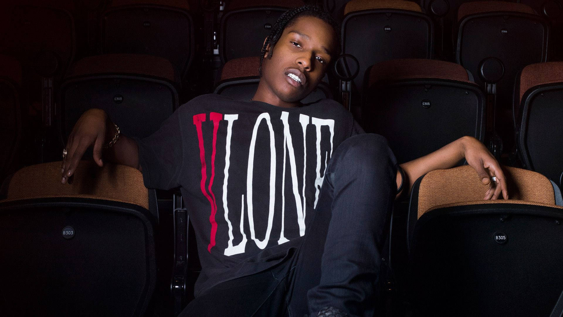 A$AP Rocky 試穿 VLONE 壁紙 — 一個穿著「LONE」T恤嘅年輕人自信咁攤喺昏暗嘅戲院座位上，散發出型格都市氣息。