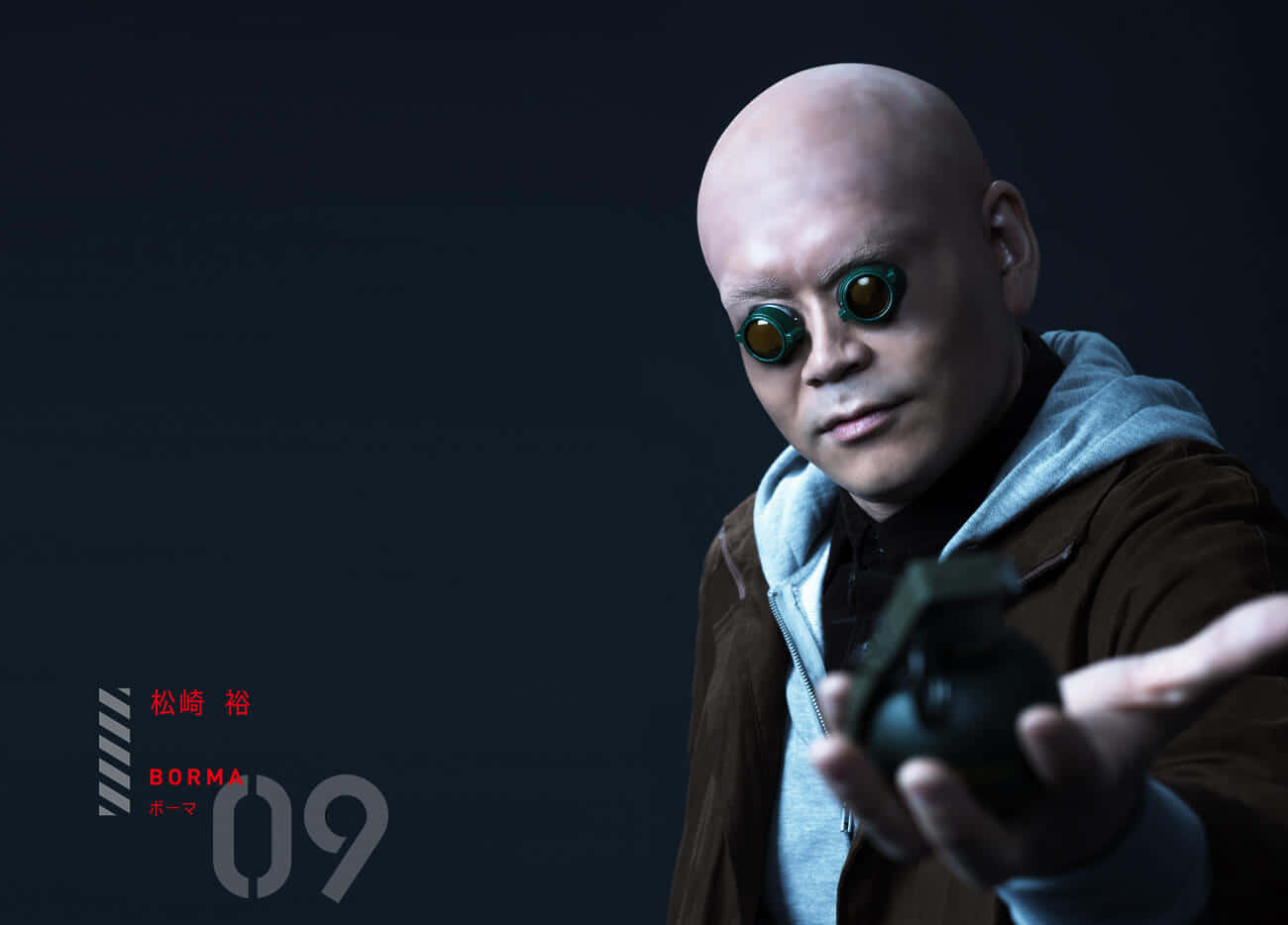  壁紙 — 一個光頭男人戴著綠色護目鏡和連帽衫，在黑暗背景下拿著手榴彈。
