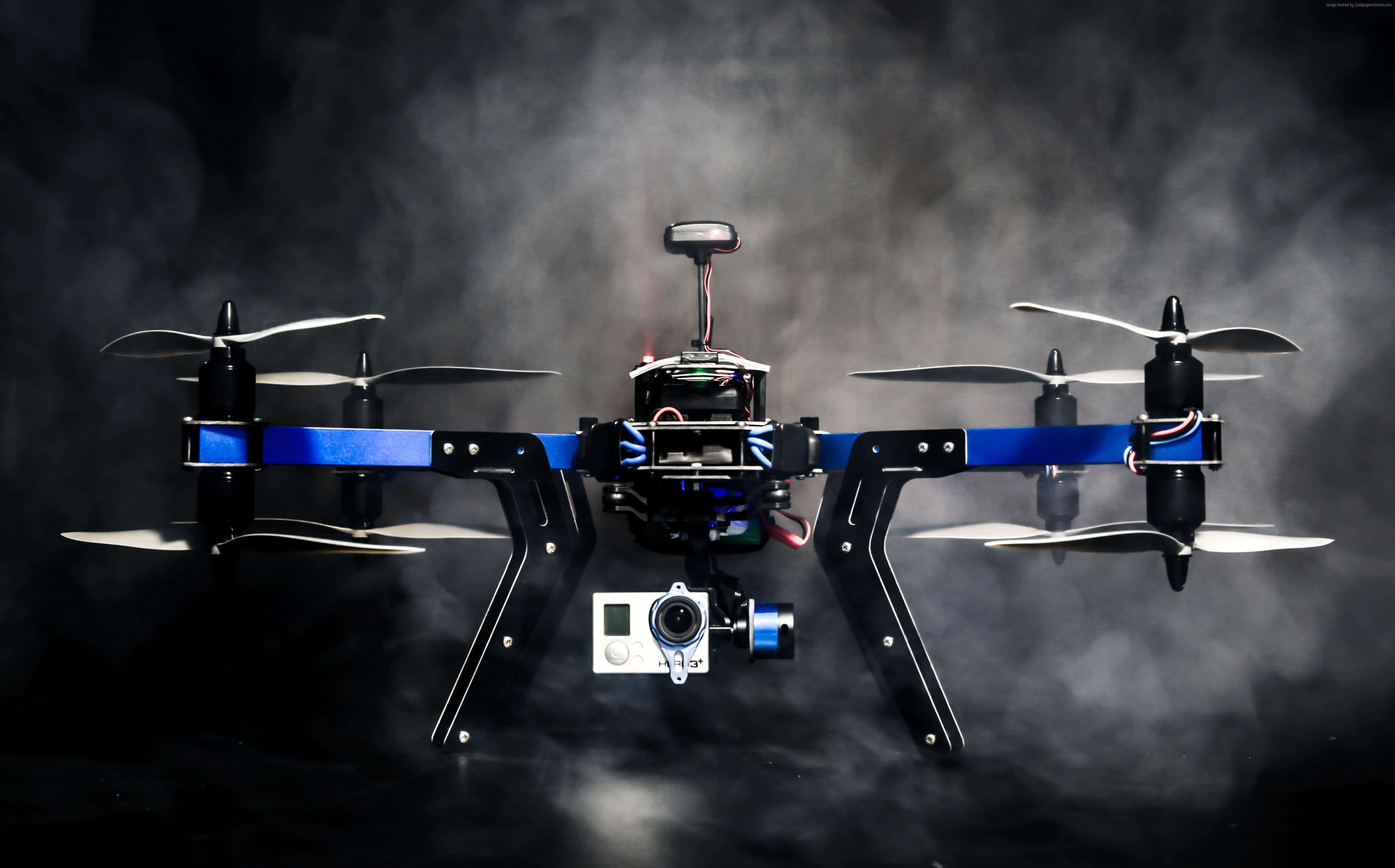 Drone Camera 桌布 壁紙 — 一部黑色和藍色的四軸無人機，帶有裸露的電線和安裝的攝像頭，在煙霧瀰漫的黑暗中盤旋。
