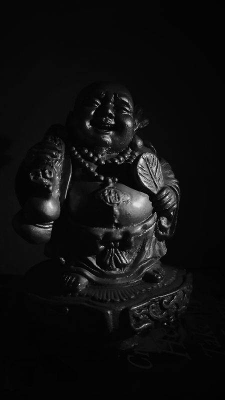 黑白微笑佛像，帶有細緻雕刻和深色背景。