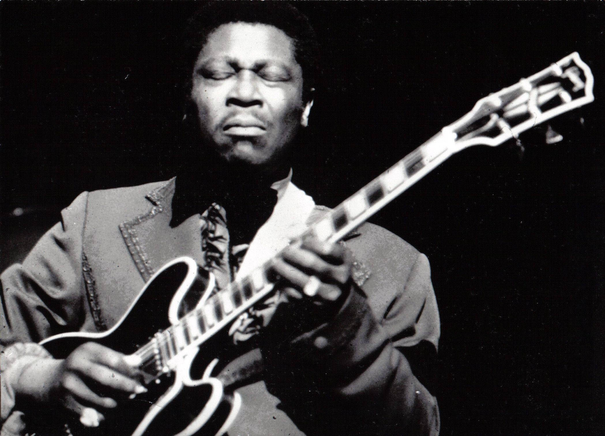 B.B. King深情表情 壁紙 — 一張黑白照片，拍攝一位音樂家在戲劇性的舞台燈光下閉著眼睛激烈地彈奏電結他。