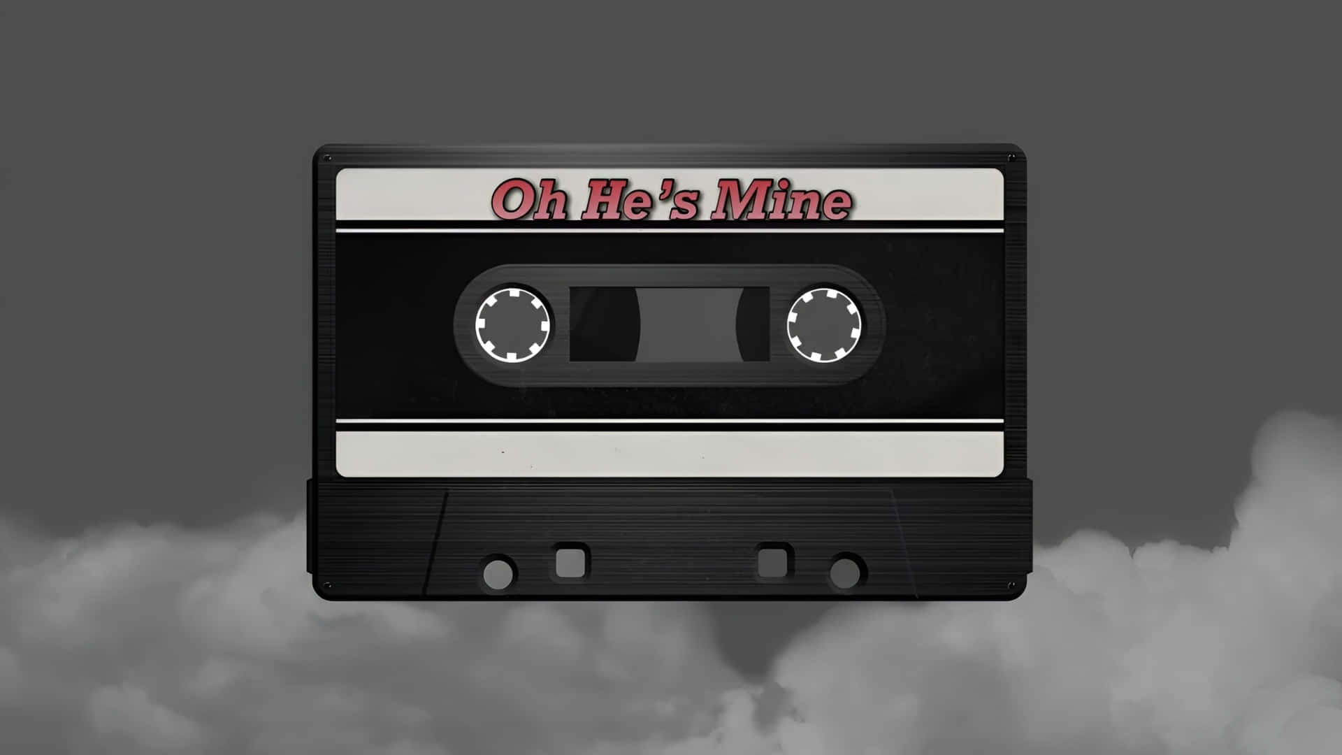  壁紙 — 一個黑色卡式錄音帶，標有 Oh He's Mine，漂浮在灰色雲層之上，背景為柔和的灰色。