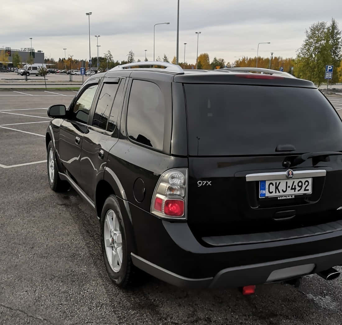 Saab 9-7x 桌布 壁紙 — 一輛黑色薩博97x SUV停泊在陰天的停車場，背景有秋天的樹木。