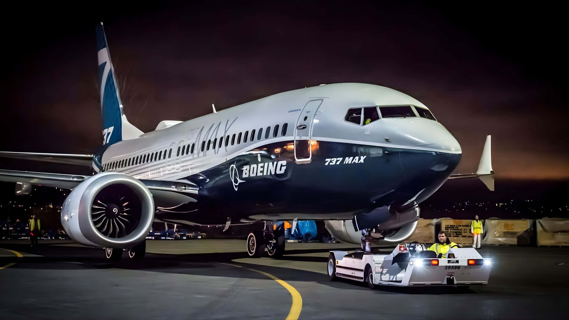  壁紙 — 一架波音737 MAX飛機在夜間被一輛明亮的拖車在機場停機坪上的人工燈光下拖行。