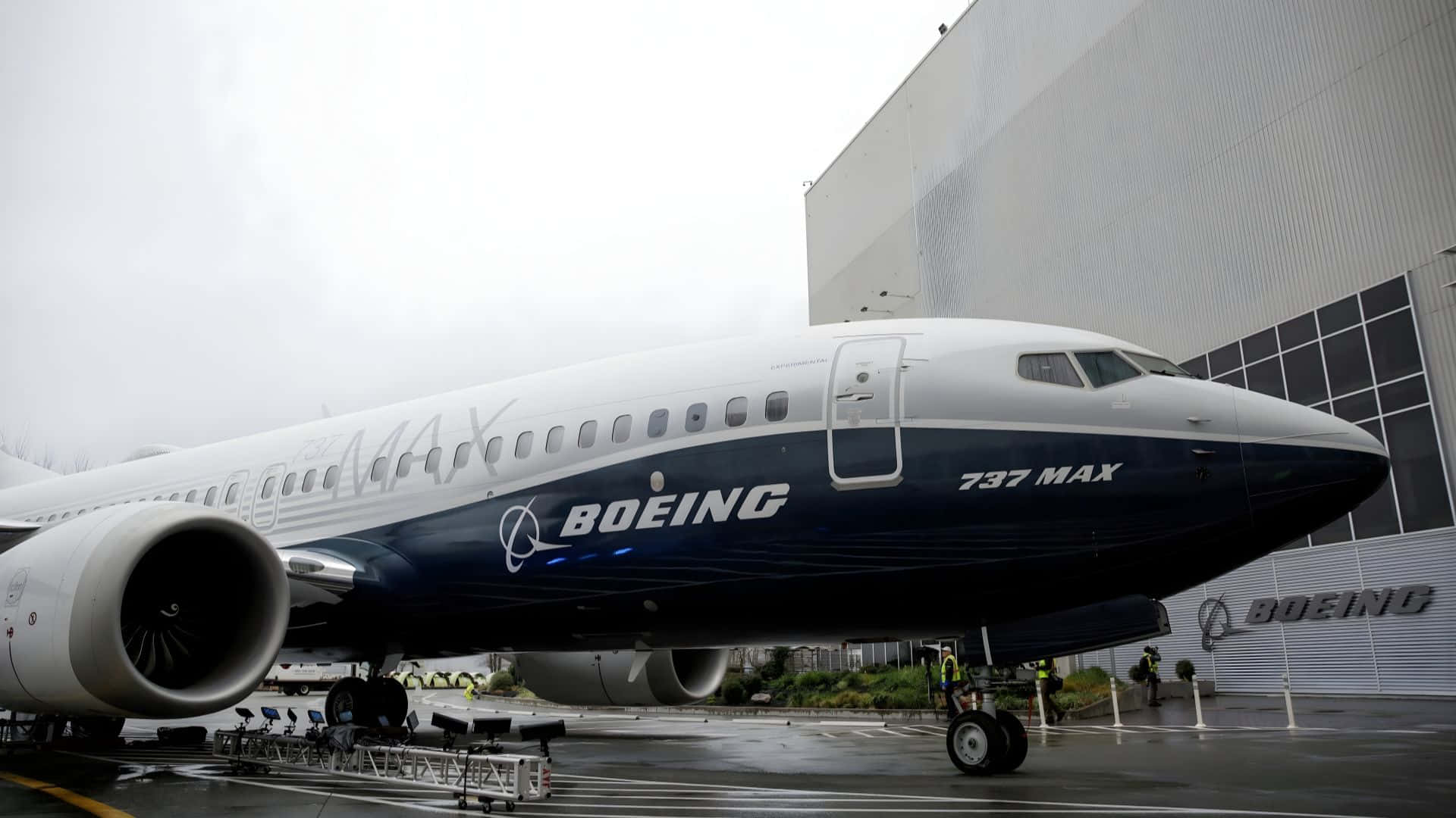  壁紙 — 一架波音737 MAX飛機停放在大型機庫外潮濕的停機坪上，天空多雲。