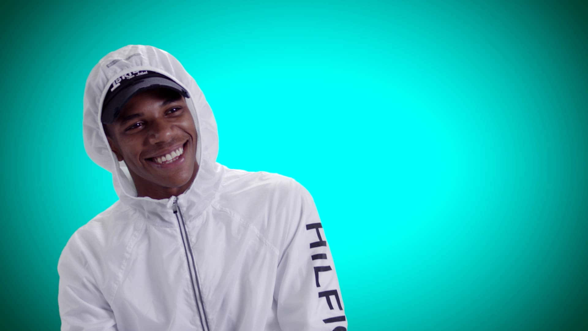 A Boogie Wit Da Hoodie 現場演出 壁紙 — 一位身穿白色連帽外套的年輕男子在充滿活力的青綠色漸變背景前燦爛微笑。