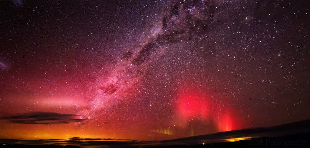  壁紙 — 令人屏息的夜空，銀河在黑暗的地平線上方閃耀著粉紅色和紫色，紅色極光在其中舞動。