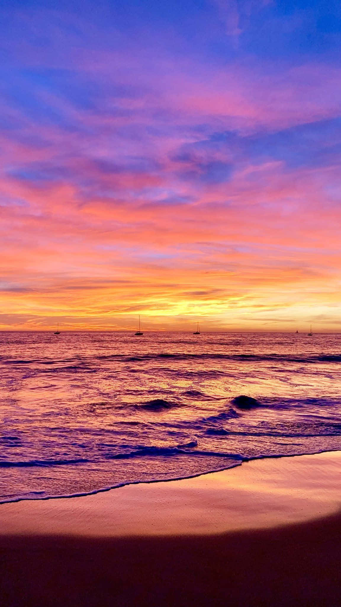 Colorful Sunset 桌布 壁紙 — 海洋上令人驚嘆的日落，充滿活力的粉紅色、橙色和紫色色調反射在水面和濕沙上，遠處有帆船。