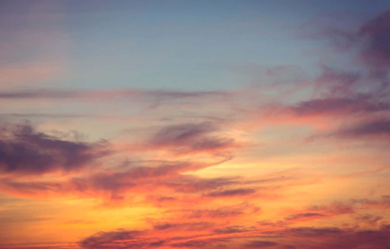 Sunset Hues 桌布 壁紙 — 令人驚嘆的日落天空，以火熱的橙色和柔和的粉紅色雲彩繪製，映襯著逐漸褪色的藍色地平線。