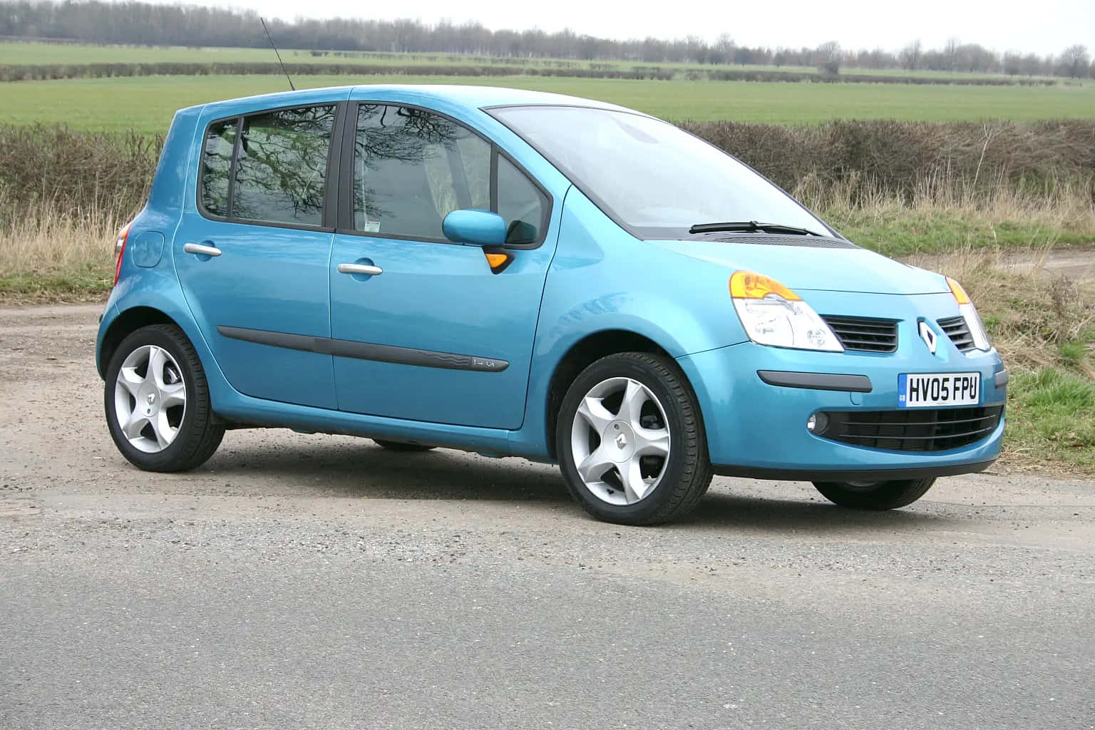 Renault Modus 桌布 壁紙 — 一輛亮藍色的雷諾 Kangoo 停泊在碎石路上，背景是綠色的田野和光禿禿的樹木。