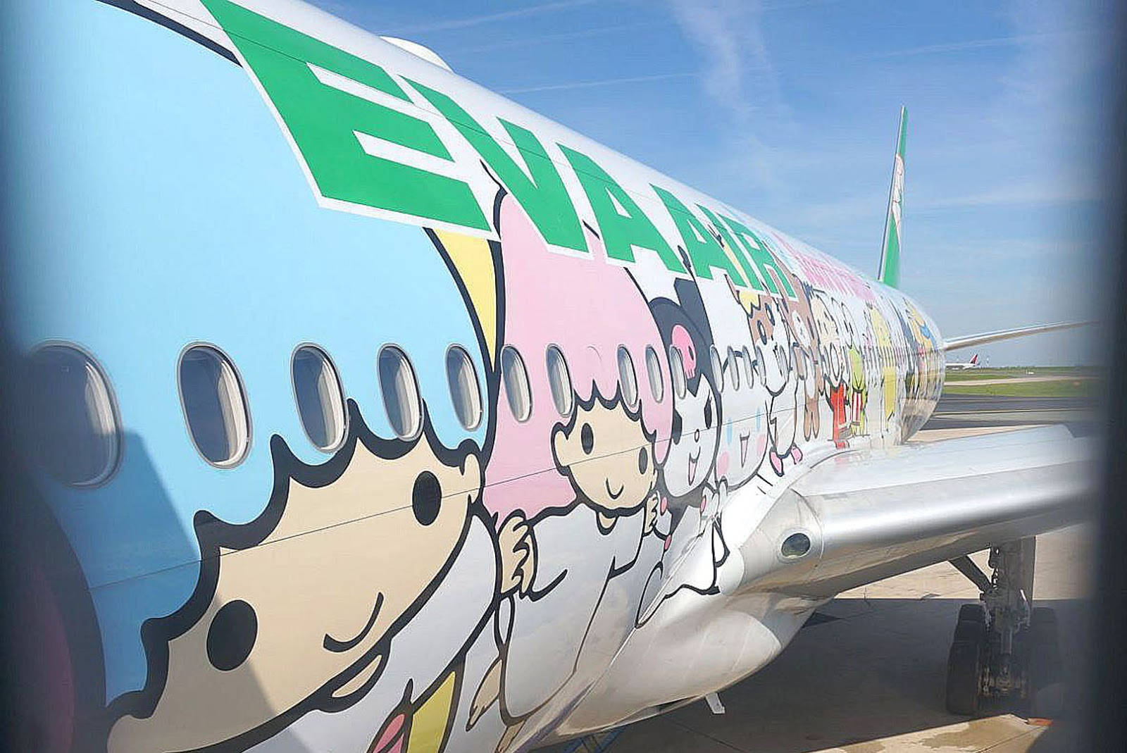 長榮航空三麗鷗角色設計 壁紙 — 在機場晴朗的藍天下，一架繪有卡通人物的鮮艷飛機機身。