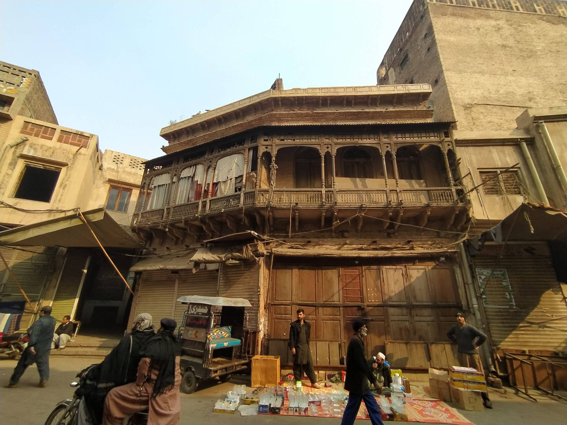 拉合爾破舊建築 壁紙 — 歷史城區的繁華街景，人們走過一棟帶陽台的風化木建築。