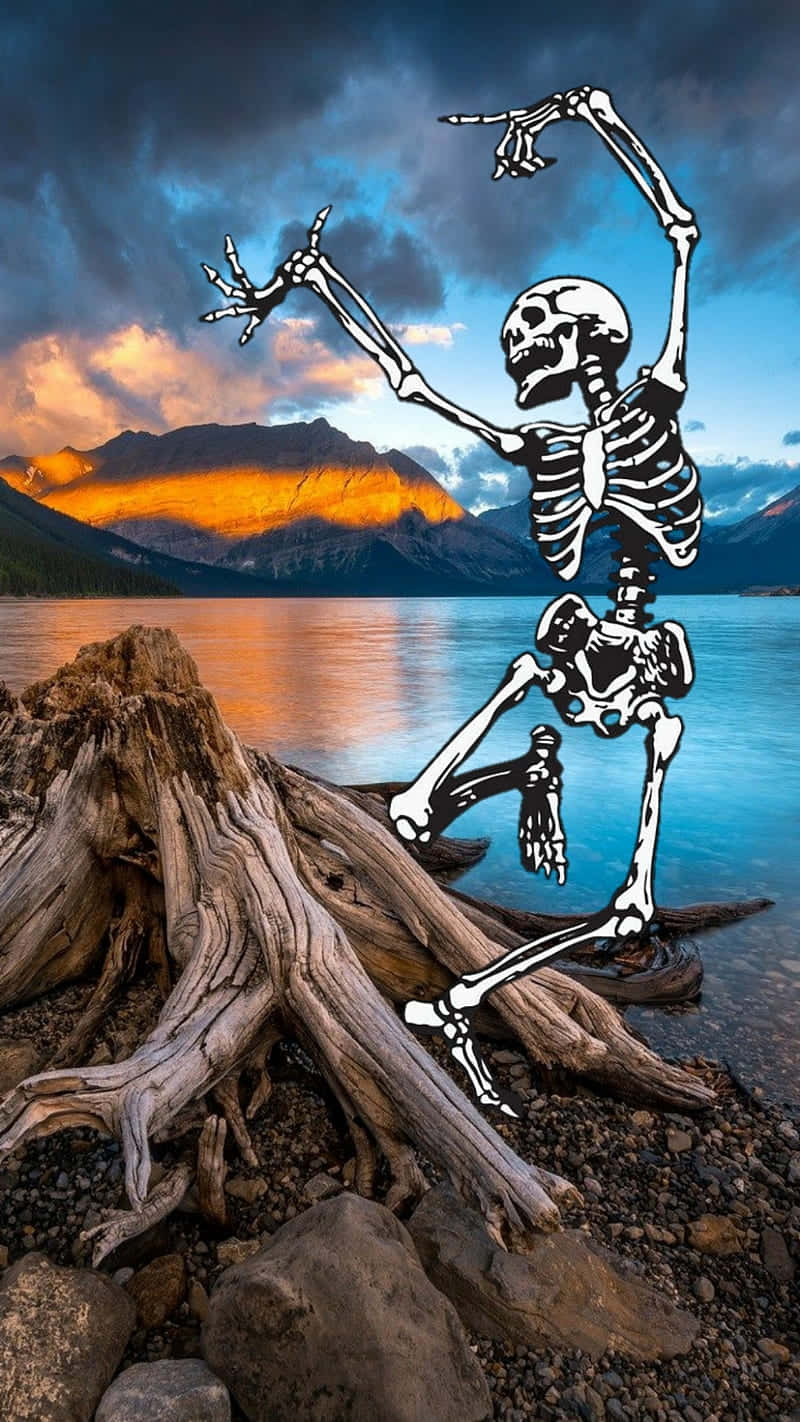  壁紙 — 一個卡通骷髏在日落時分在湖岸上快樂地跳舞，背後山巒閃耀。