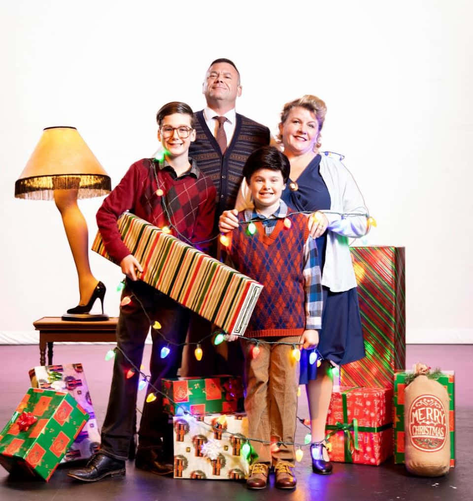 《A Christmas Story》電影Parker一家 壁紙 — 一家人愉快地擺姿勢，拿著超大的聖誕禮物和節日燈飾，圍繞著桌上的燈。