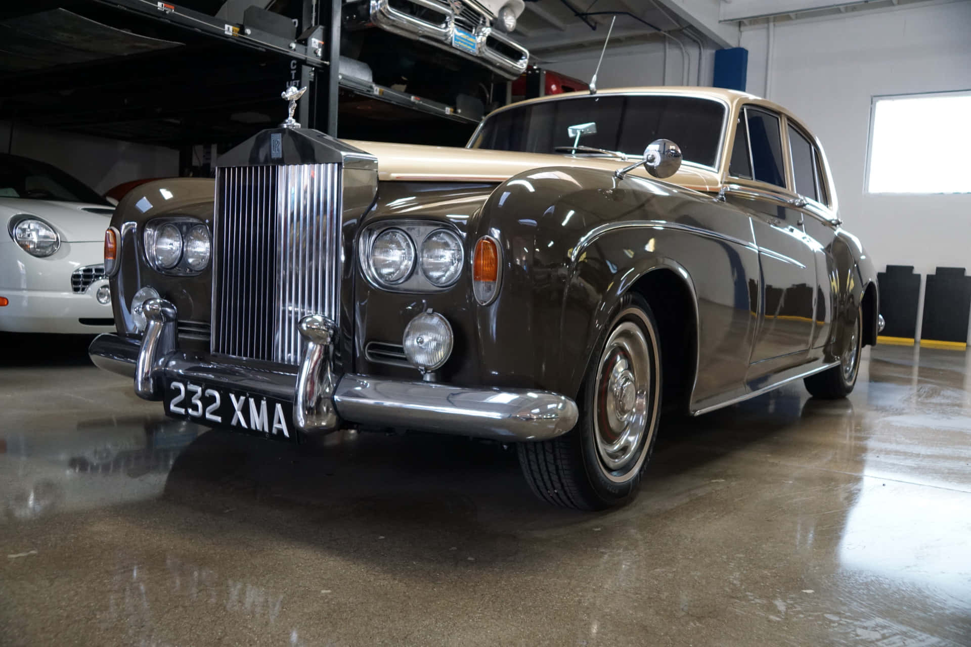 Bentley S3 桌布 壁紙 — 經典深綠色勞斯萊斯，鍍鉻飾邊在明亮的車庫燈光下閃閃發光，停在一輛白色跑車旁邊。