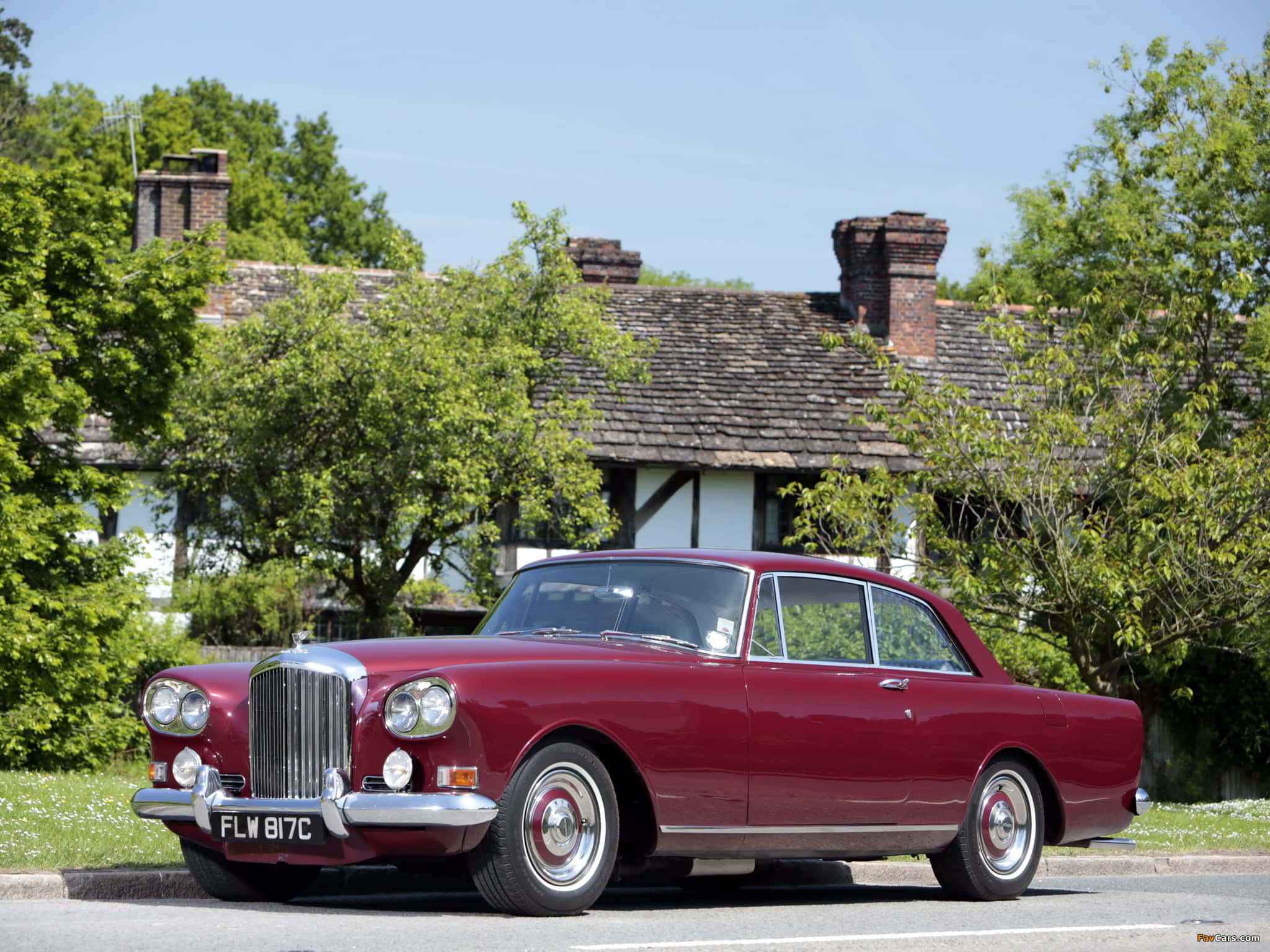 Bentley S3 桌布 壁紙 — 一輛經典的栗色賓利S1在陽光明媚的日子裡停在一棟傳統木結構房屋前，周圍環繞著茂密的綠樹。