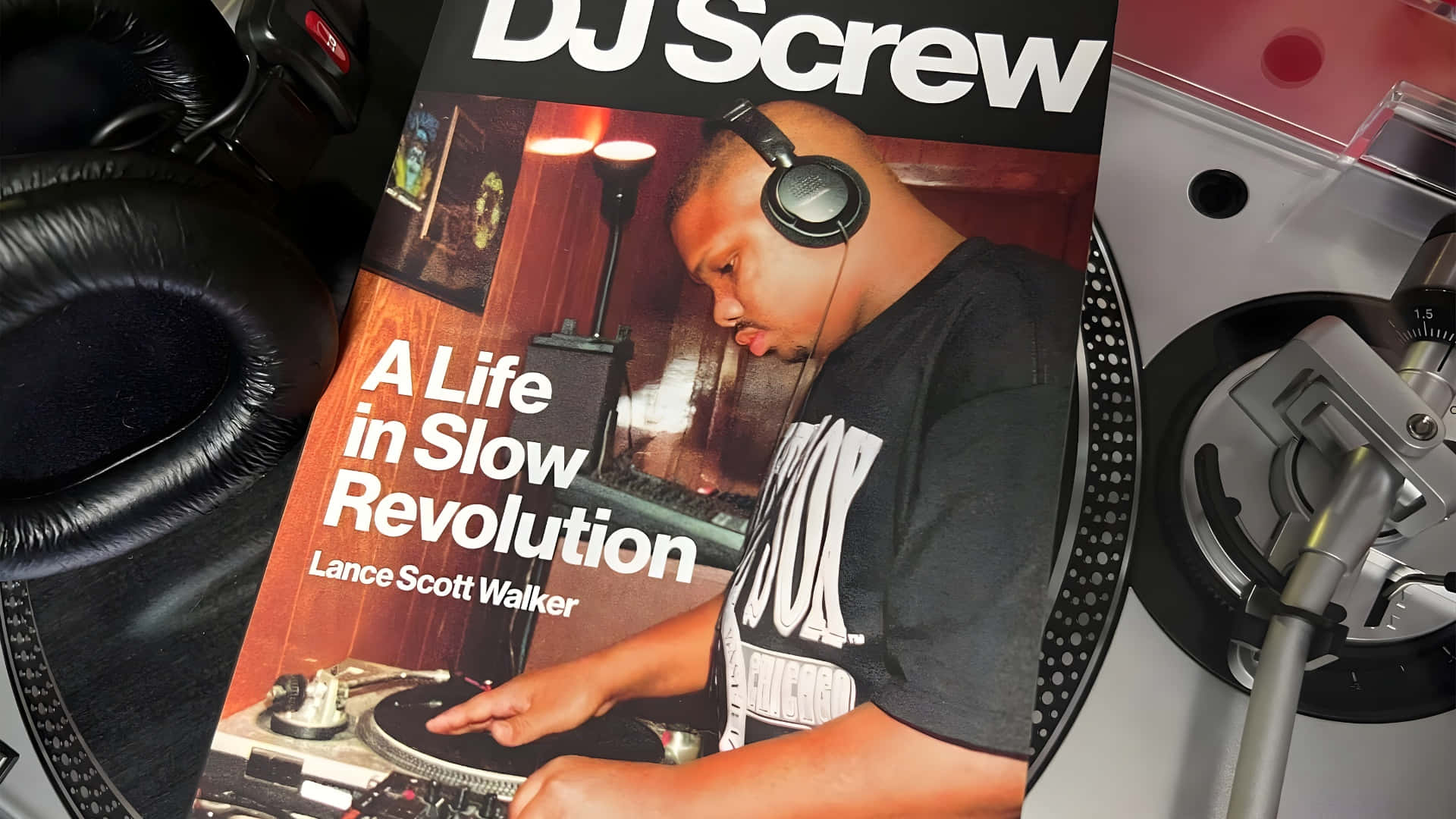  壁紙 — DJ Screw 傳記書的特寫，放在唱盤上，周圍有耳機和黑膠唱片。