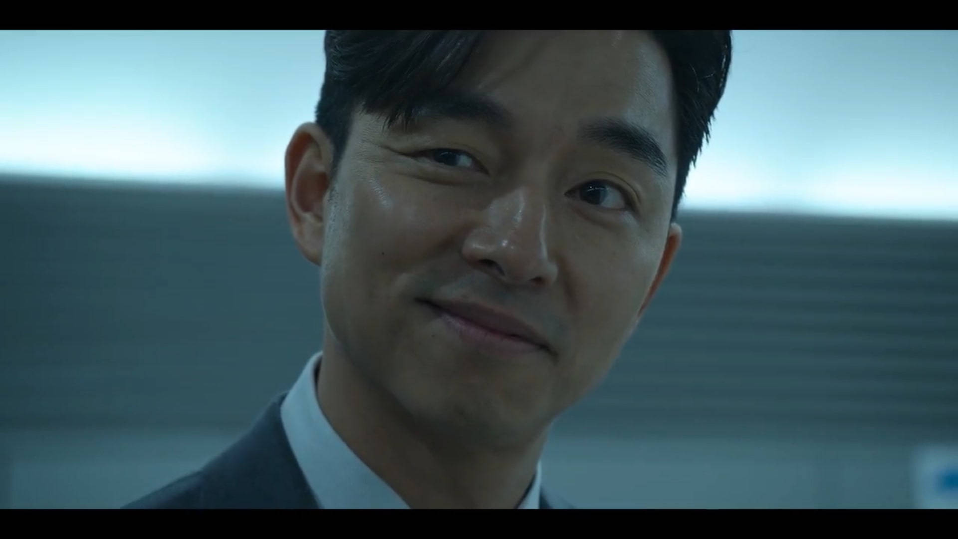 《魷魚遊戲》孔劉 壁紙 — 一名身穿西裝的男子在冷色調模糊背景前微妙微笑的特寫。