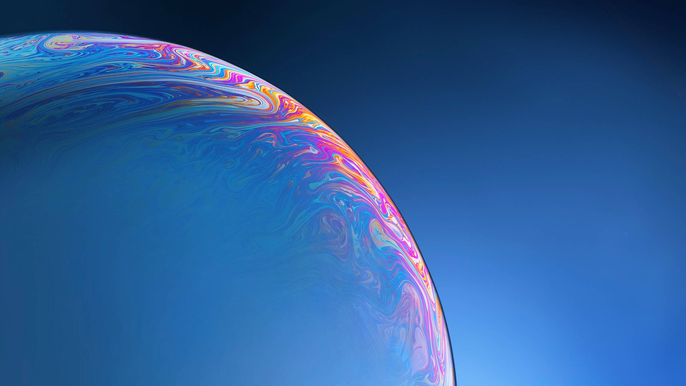 iPhone 水珠表面特寫 壁紙 — 肥皂泡的特寫，帶有旋轉的彩虹色，背景是漸變藍天。