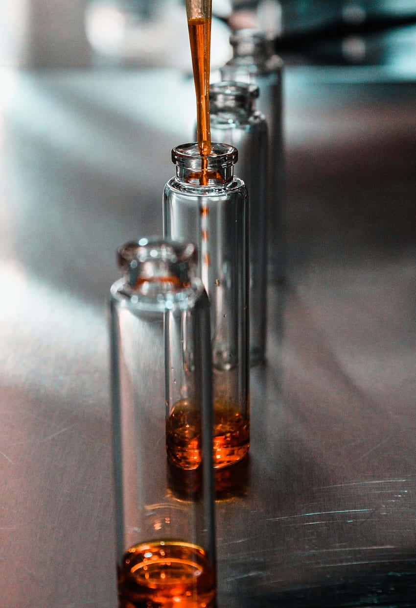  壁紙 — 琥珀色液體滴入排列在拉絲金屬表面上的透明玻璃瓶的特寫。