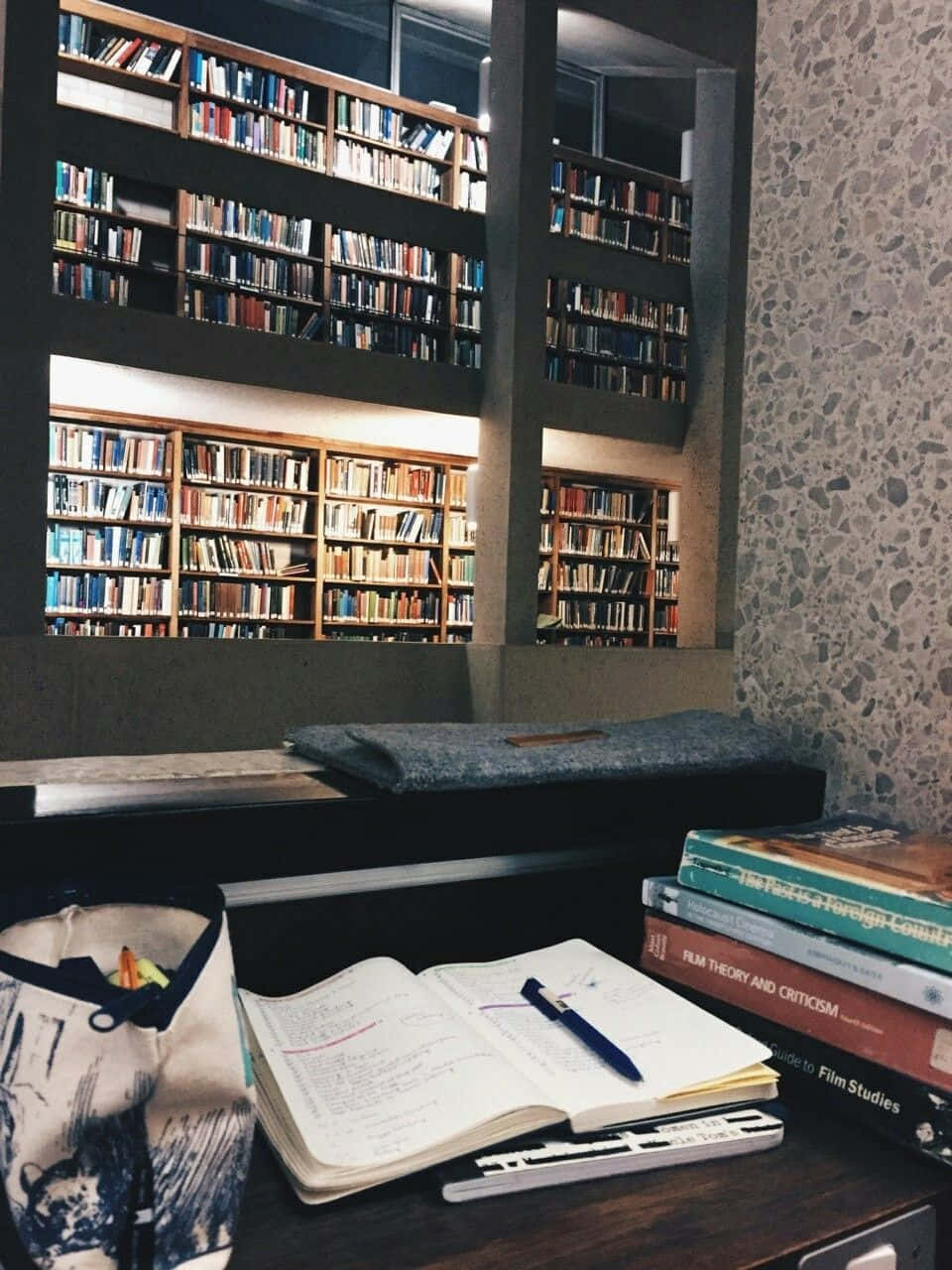  壁紙 — 一個舒適的閱讀角落，放著一本打開的筆記本、筆和書籍，旁邊是高聳的書架，擺滿了色彩繽紛的書脊。
