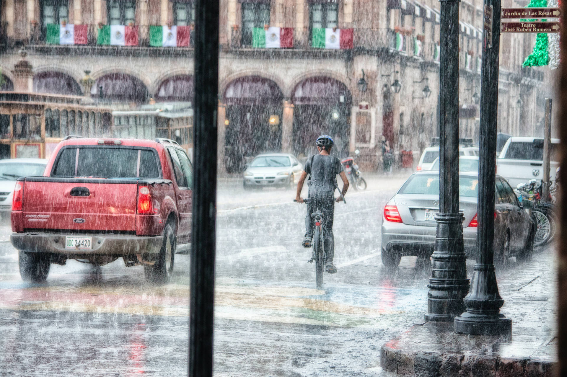 騎單車的人在繁忙的城市街道上冒著大雨騎行，周圍有汽車和歷史建築。